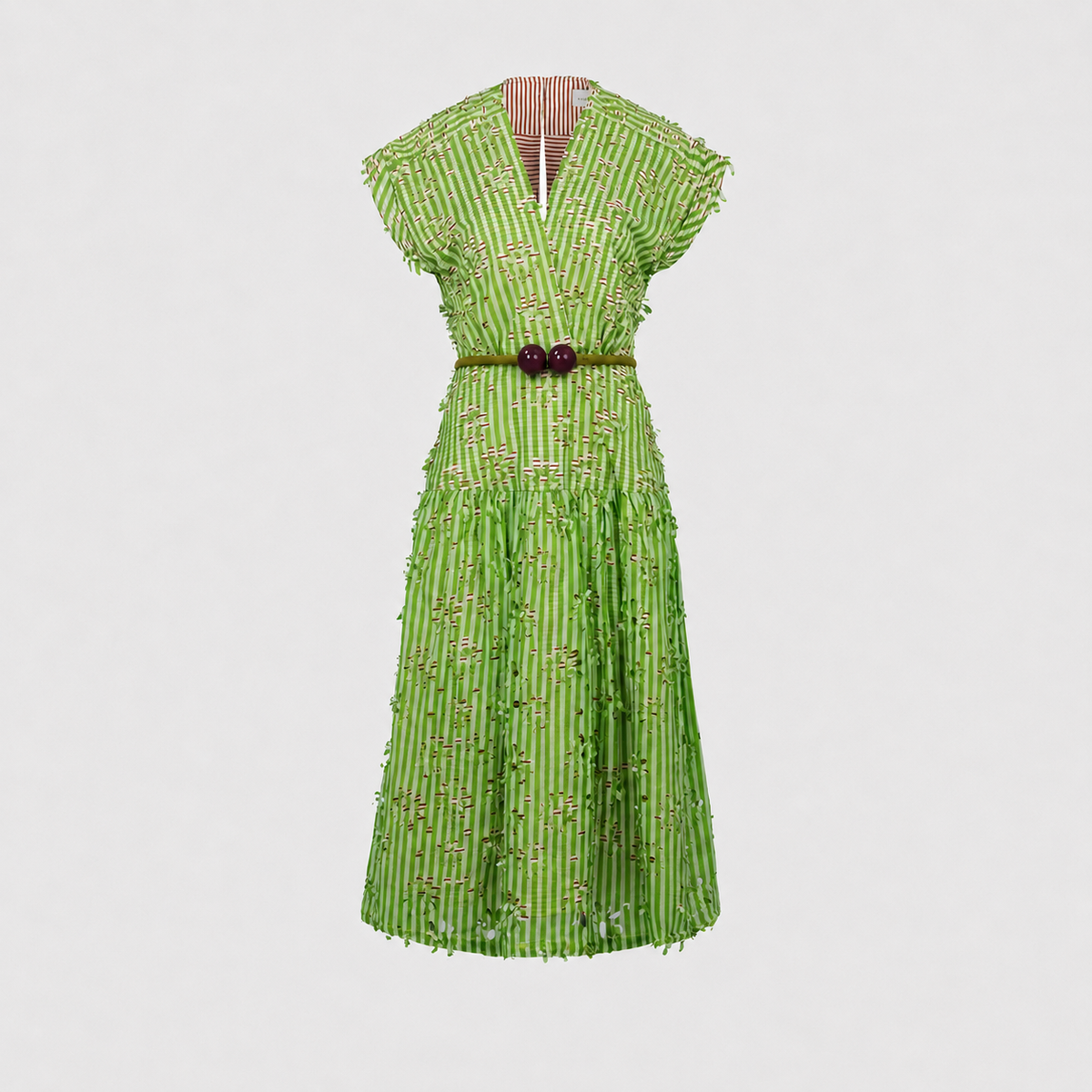 The Ledicia Dress is a green, short-sleeved dress with a V-neckline, a red-striped inner lining, and a belted waist featuring a red buckle. It is adorned with small embellishments throughout.