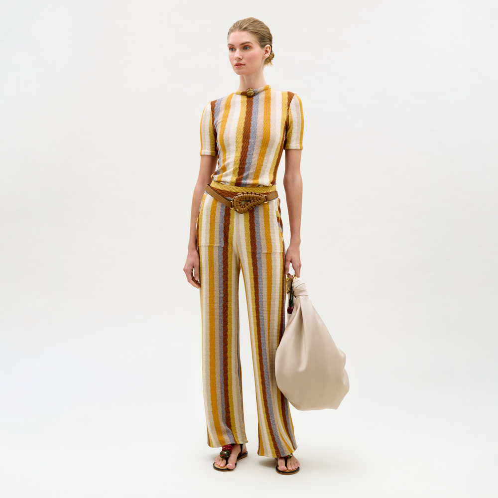 Woman wearing a striped outfit holding a beige bag on a white background