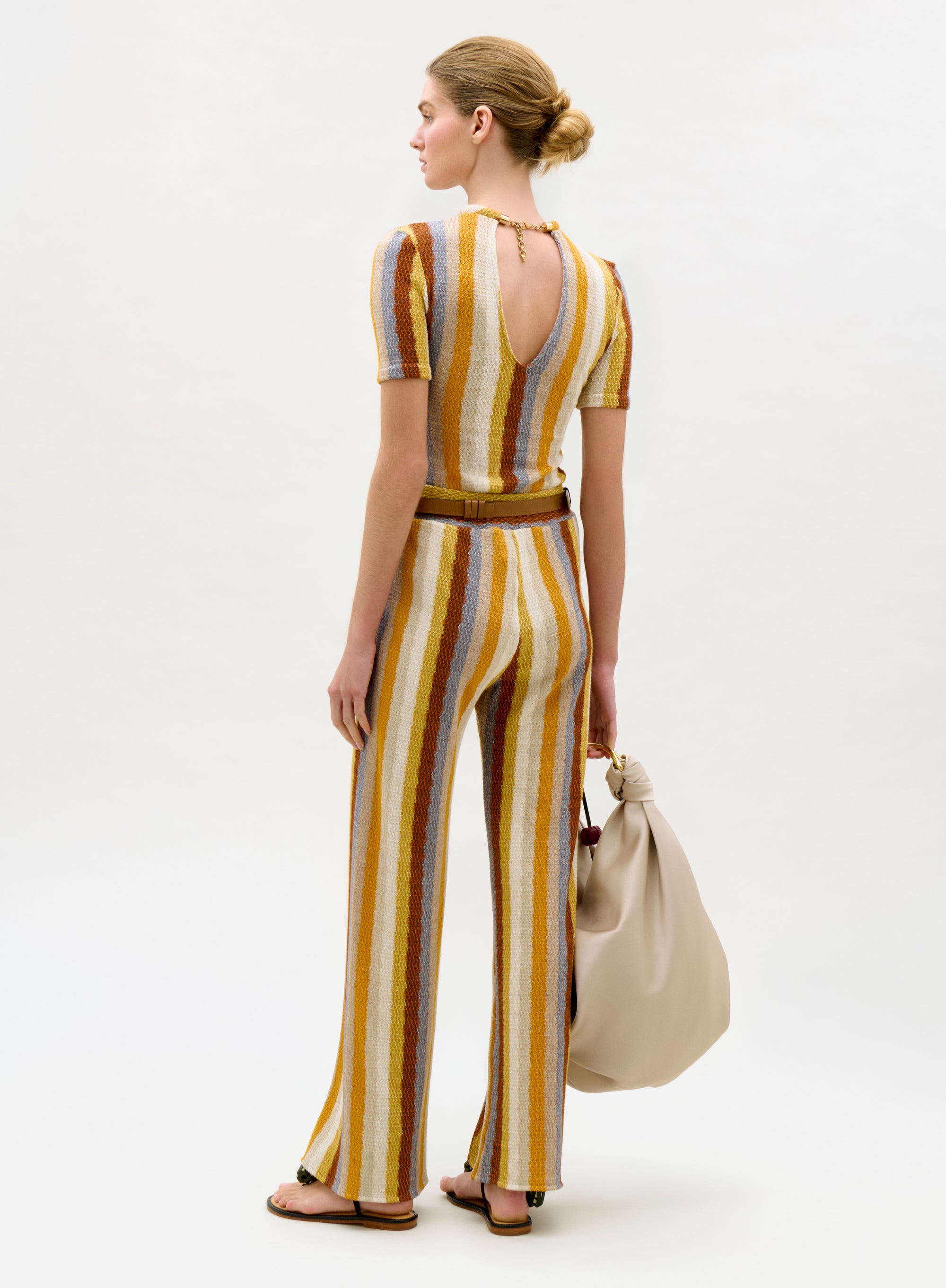 Woman wearing a striped jumpsuit holding a beige handbag on a white background
