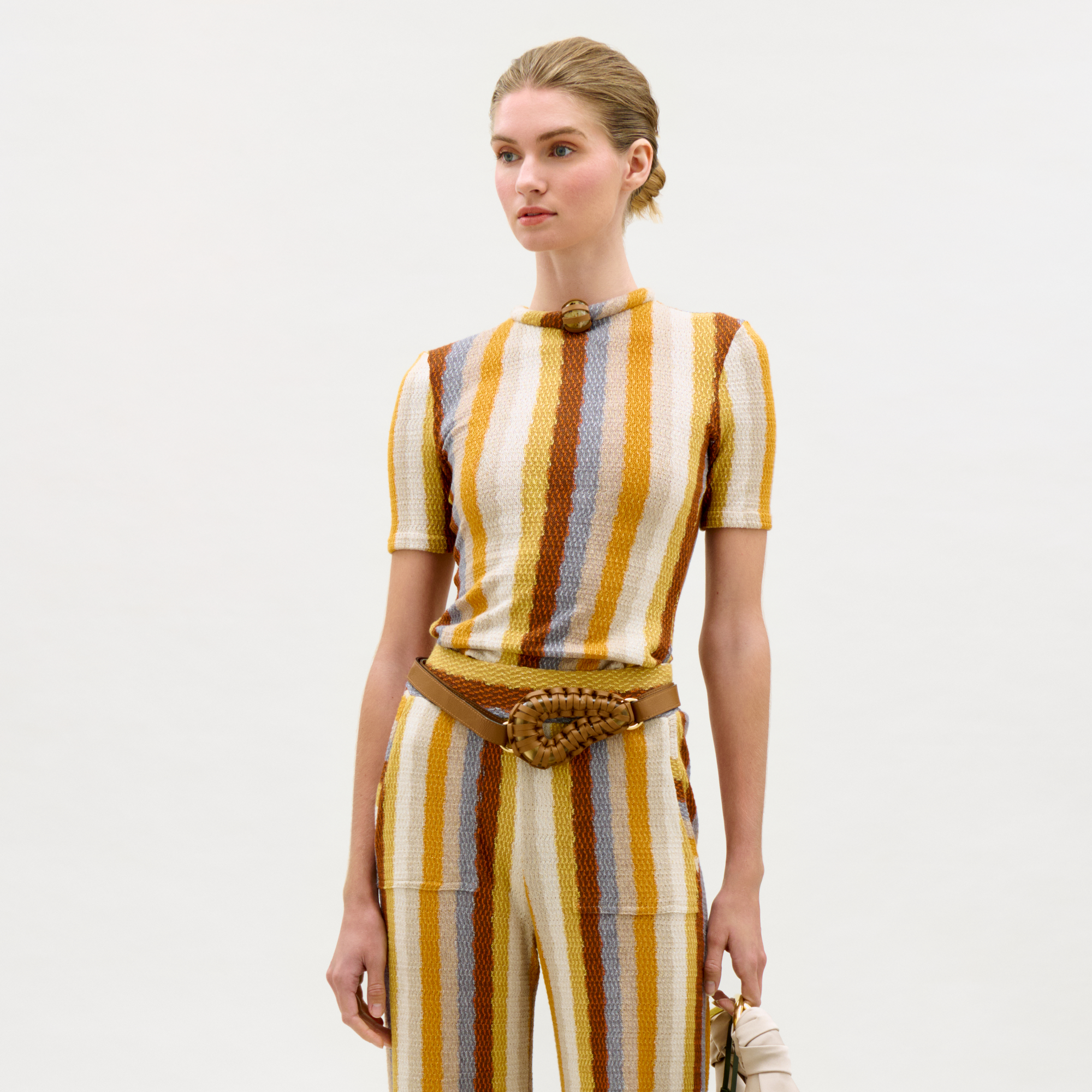 Woman wearing a striped outfit with a belt on a light gray background