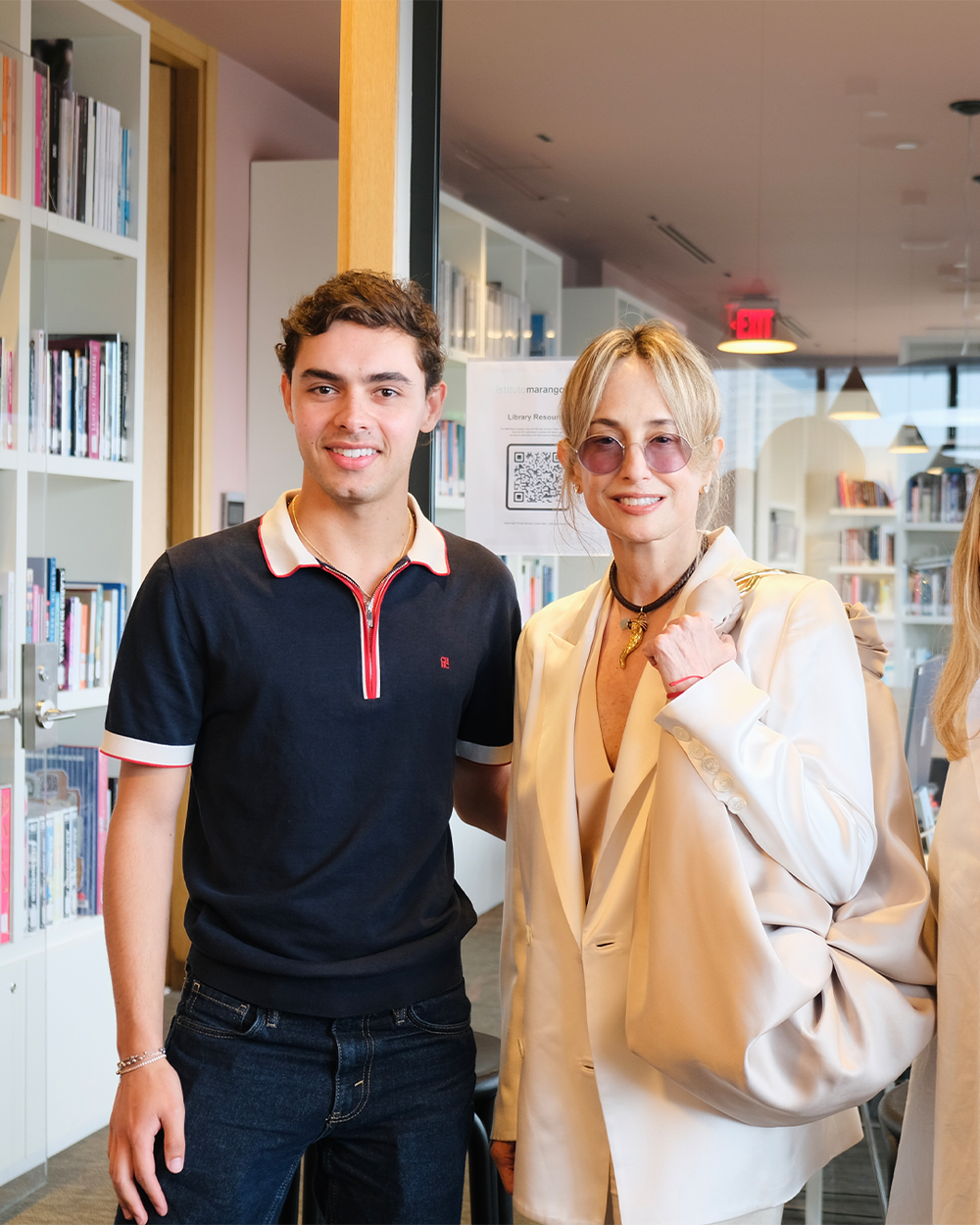 Two people standing in a library or bookstore with bookshelves in the background.