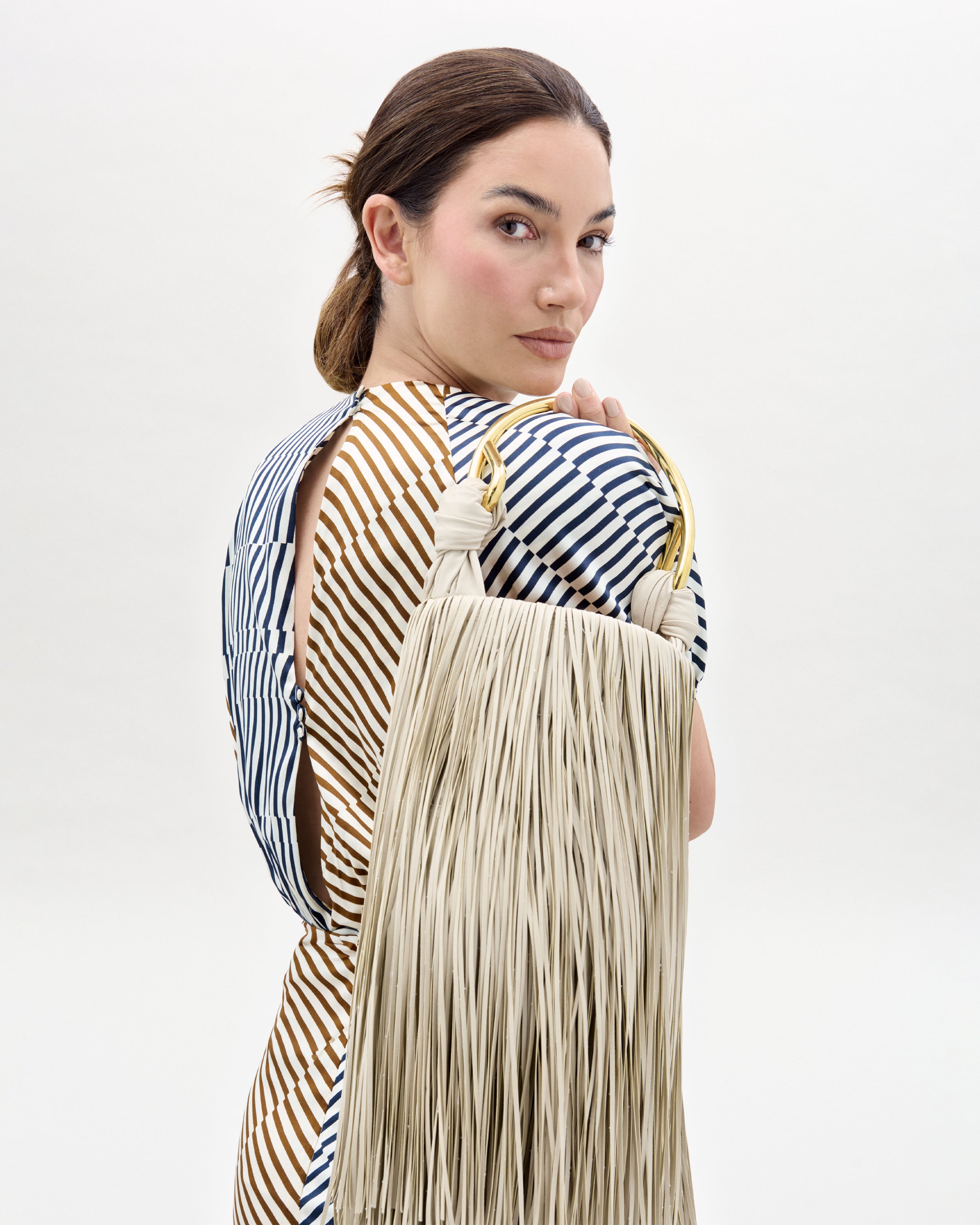 Woman holding a beige handbag with long fringes against a white background