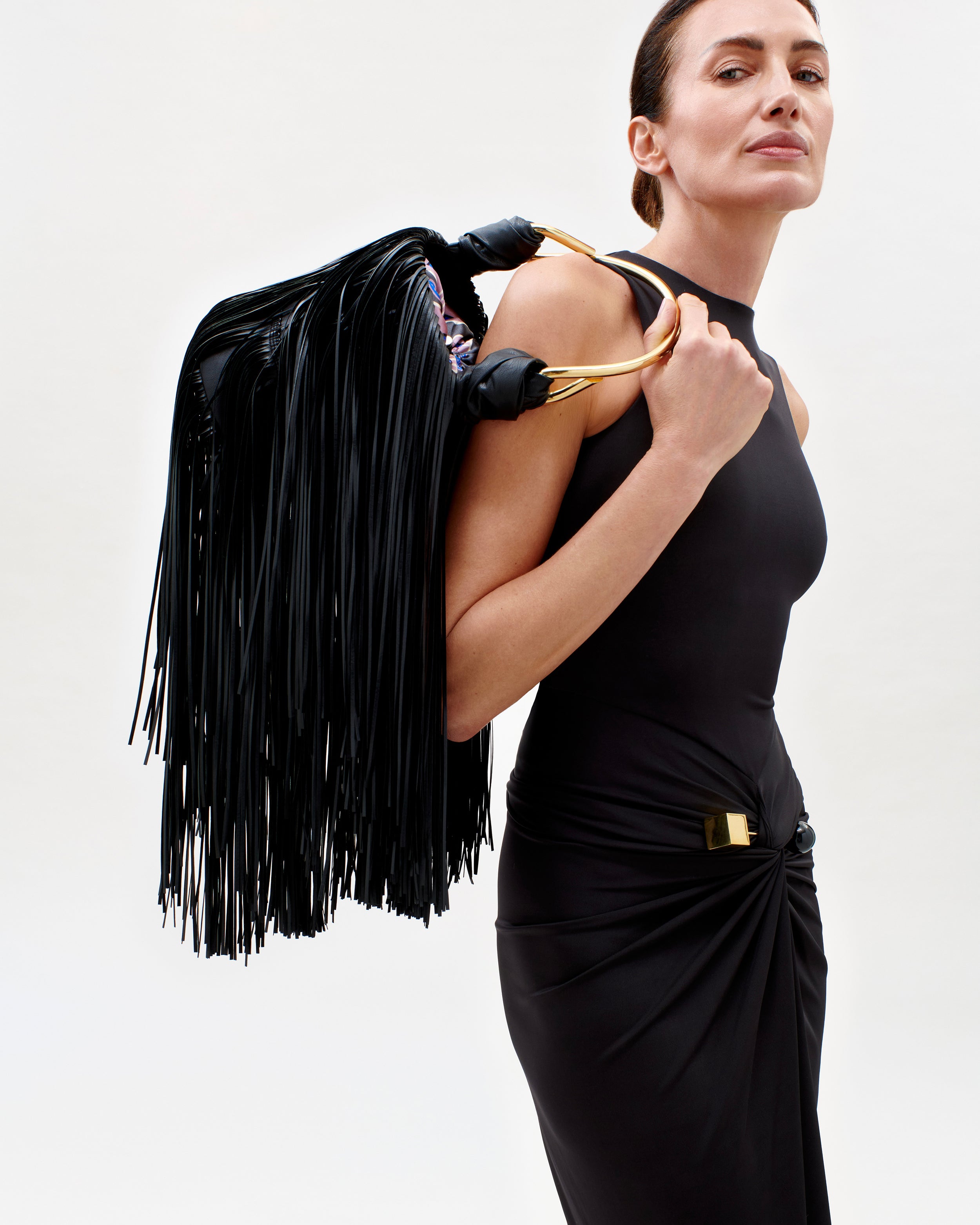 The Supermodel Nieves Alvarez holding a black leather handbag with gold accents against a white background