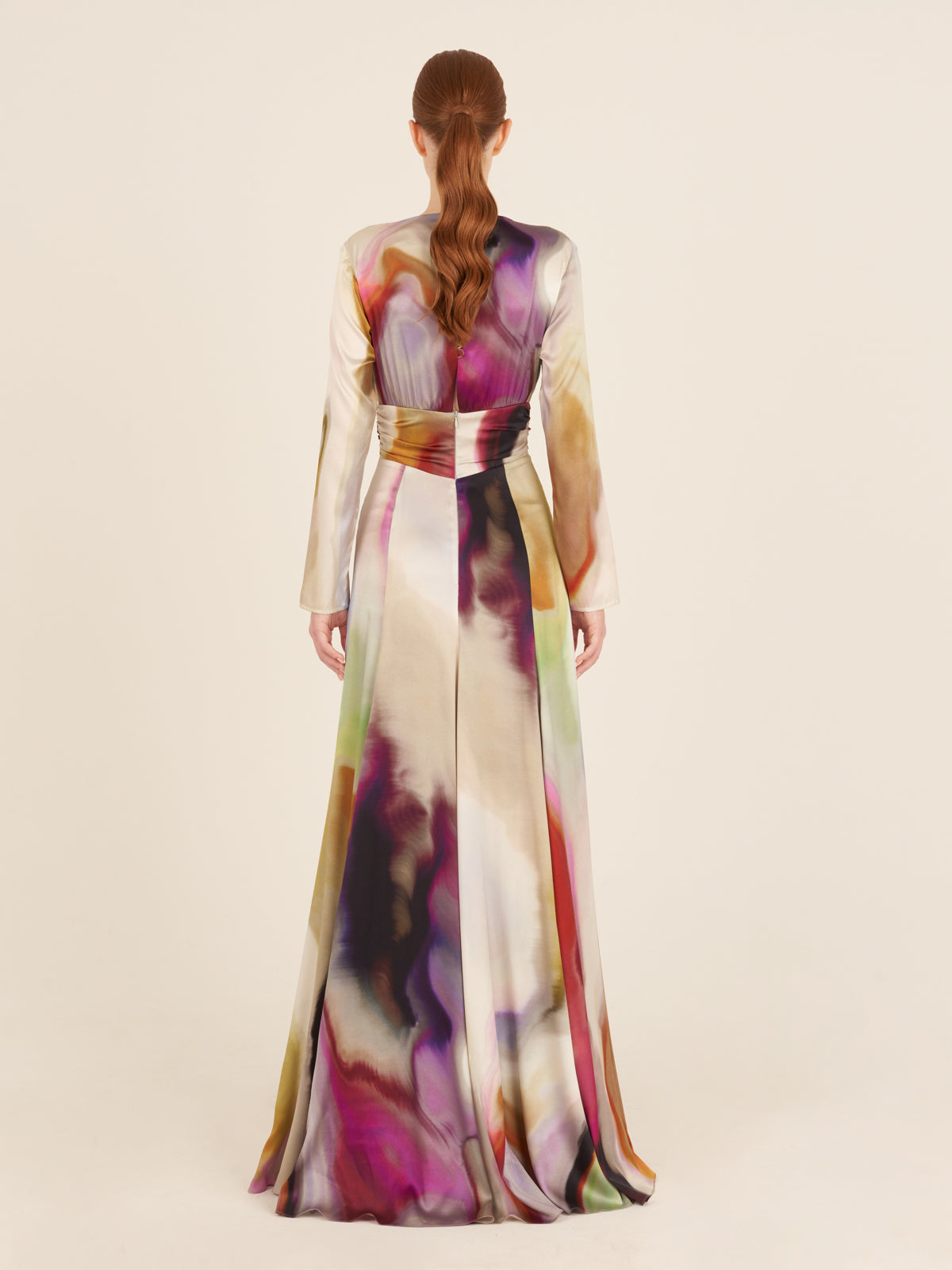 The Zarina Dress Iridescent Marble is a long-sleeve maxi dress made from luxurious Italian silk, showcasing a vibrant iridescent marble pattern with a cinched waist and a circular detail at the center.