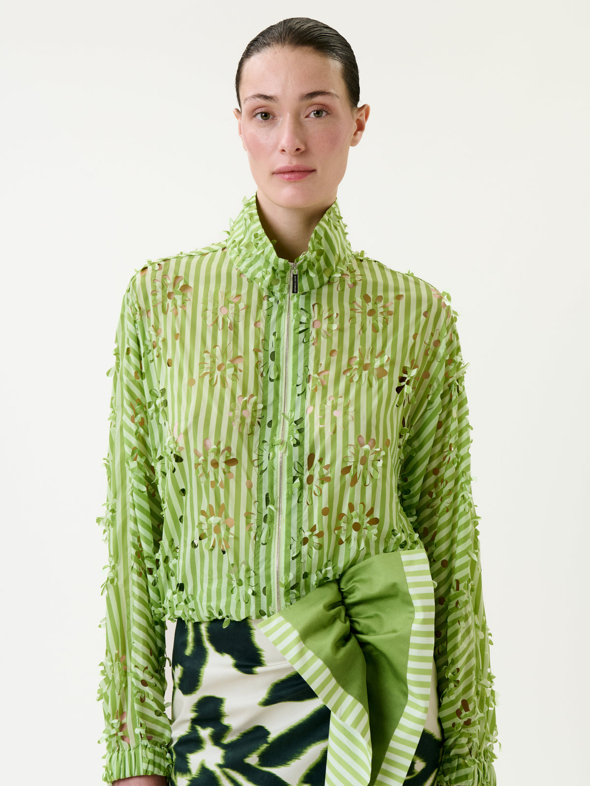A person wearing the Randy Jacket, a sheer green striped blouse with floral embroidery, paired with a green and white patterned skirt, standing against a plain white background.