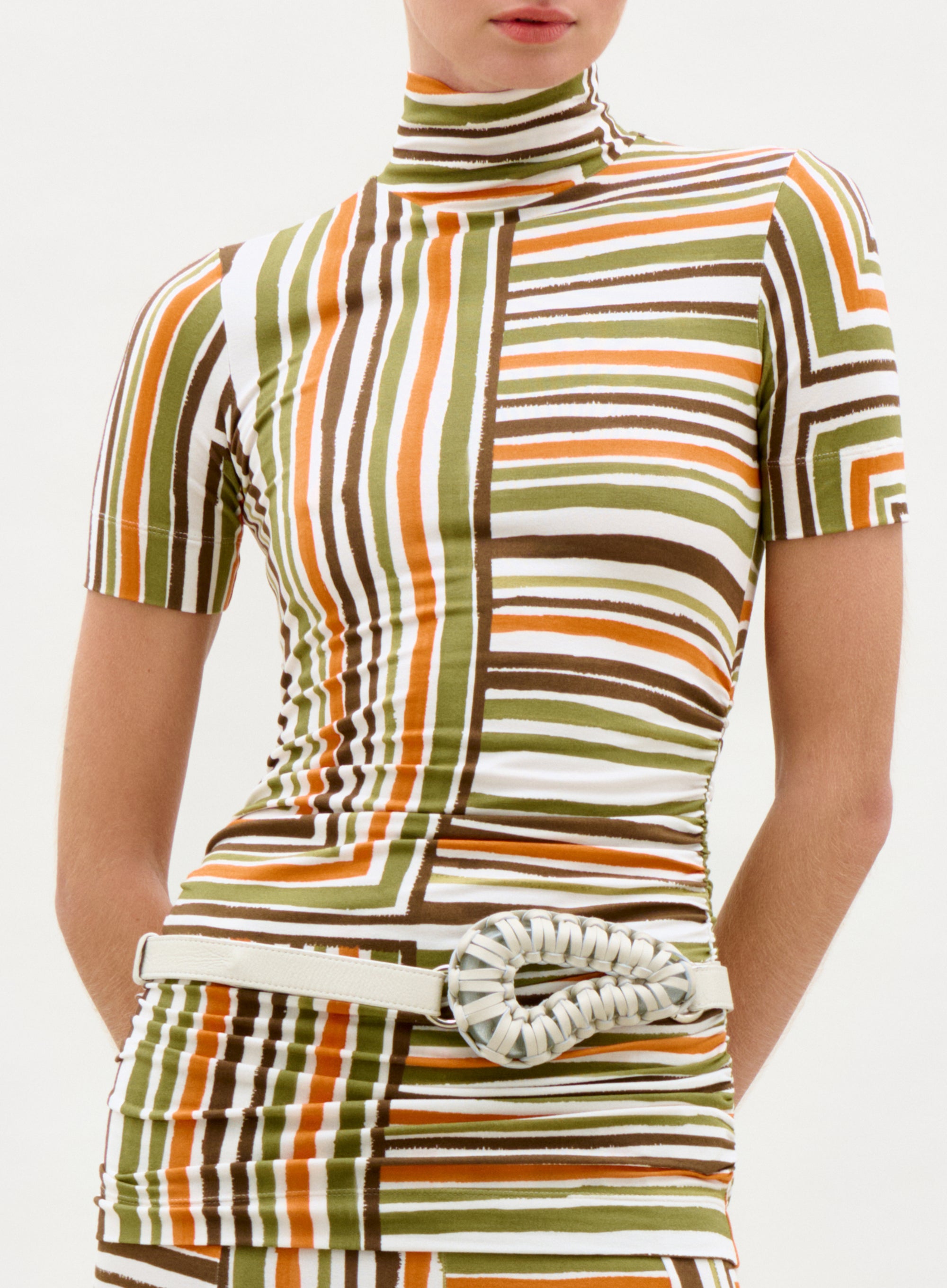 Person wearing a patterned dress with a white belt on a plain background