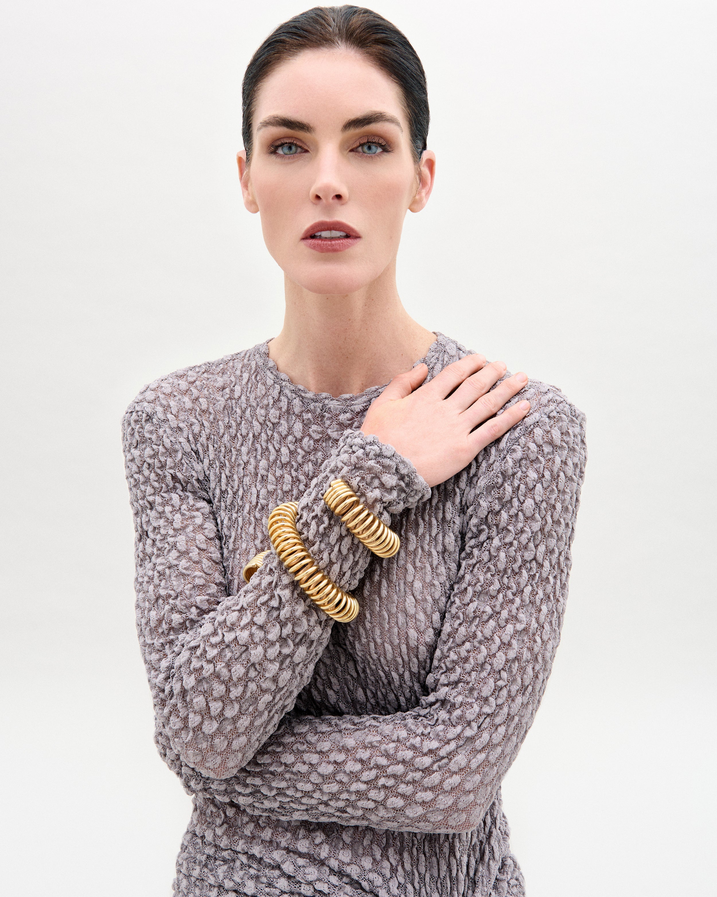 Woman wearing a textured gray sweater with gold bangles on a white background