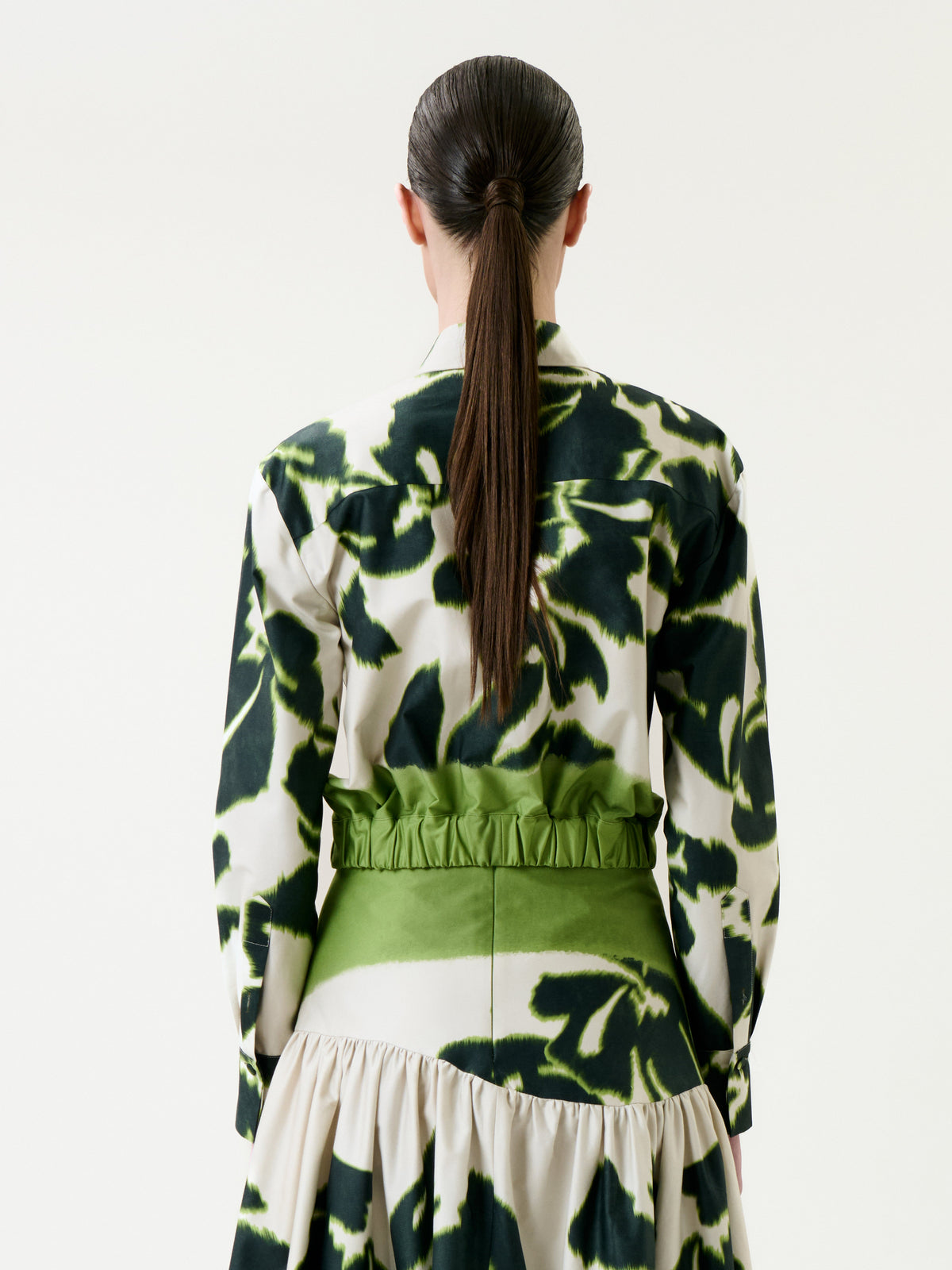 A woman with long, straight brown hair in a ponytail is seen from the back against a plain white background, wearing the Soleil Jacket.