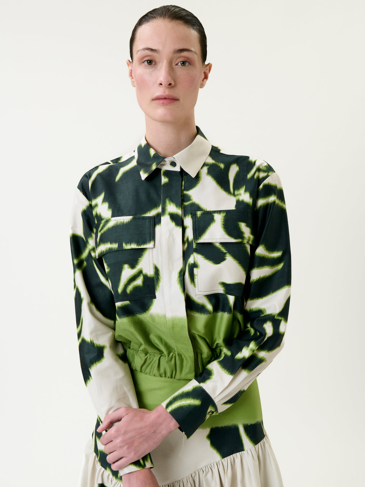 A person with slicked-back hair wears the Soleil Jacket, a green and white patterned collared shirt with front pockets, standing against a plain light background.