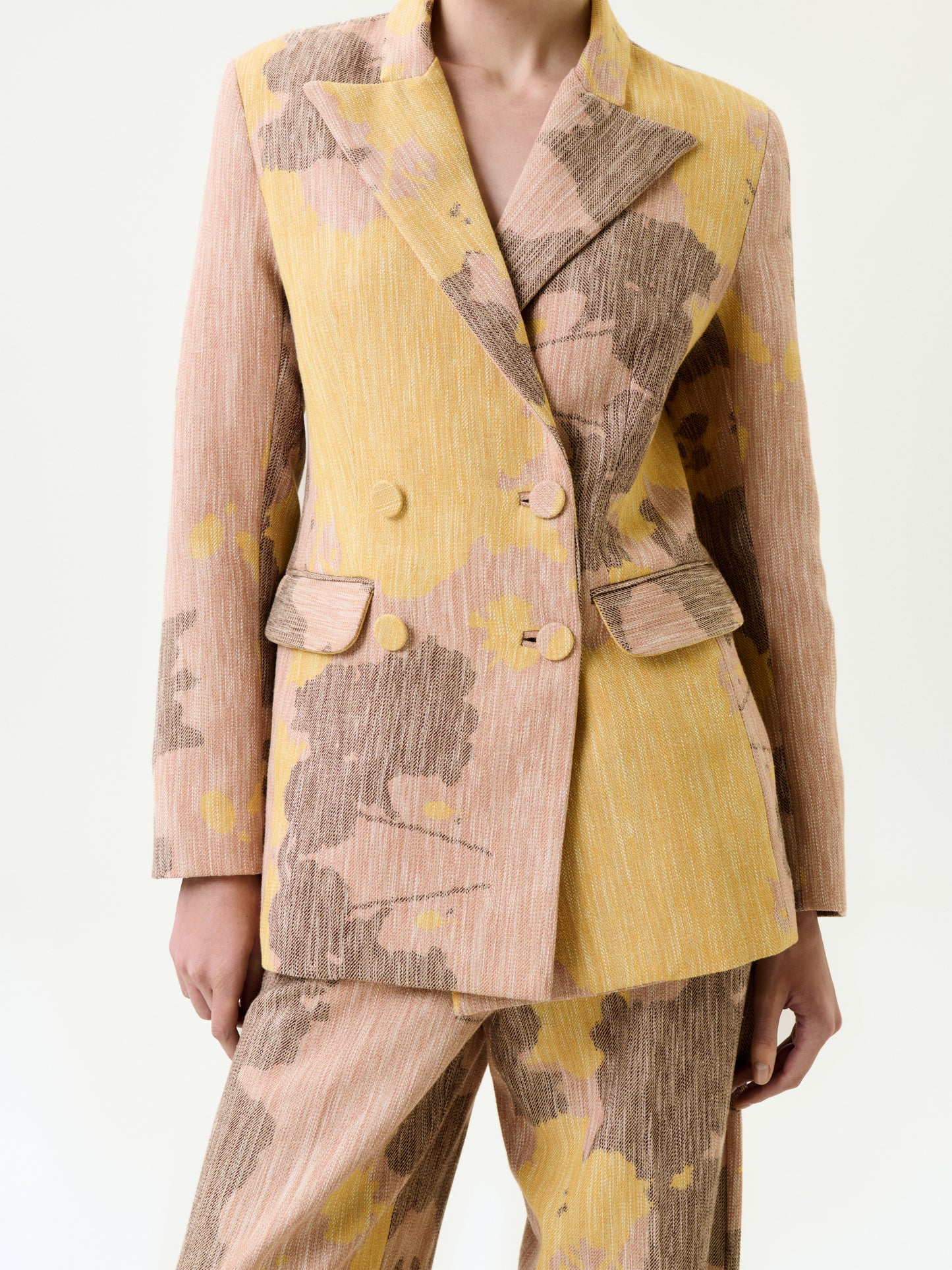 A person wearing the Frankie Jacket, a textured double-breasted suit in light pink, yellow, and brown abstract Italian fabric with flap pockets and wide lapels. The true-to-size jacket is paired with matching pants for a complete look.