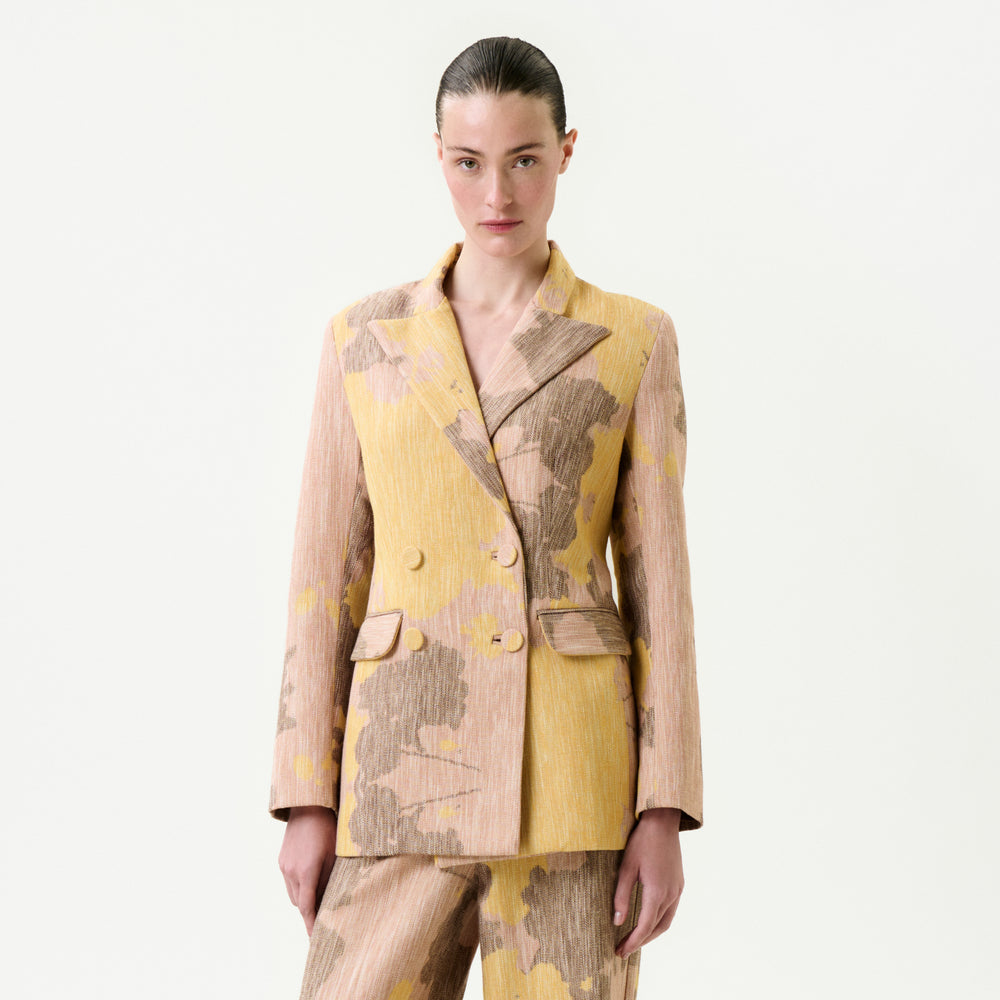 A person with slicked-back hair models the Frankie Jacket—yellow and beige floral Italian fabric, true to size—with matching pants, posing against a white background.