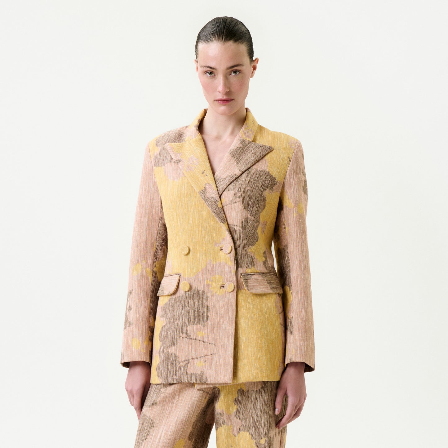 A person with slicked-back hair models the Frankie Jacket—yellow and beige floral Italian fabric, true to size—with matching pants, posing against a white background.