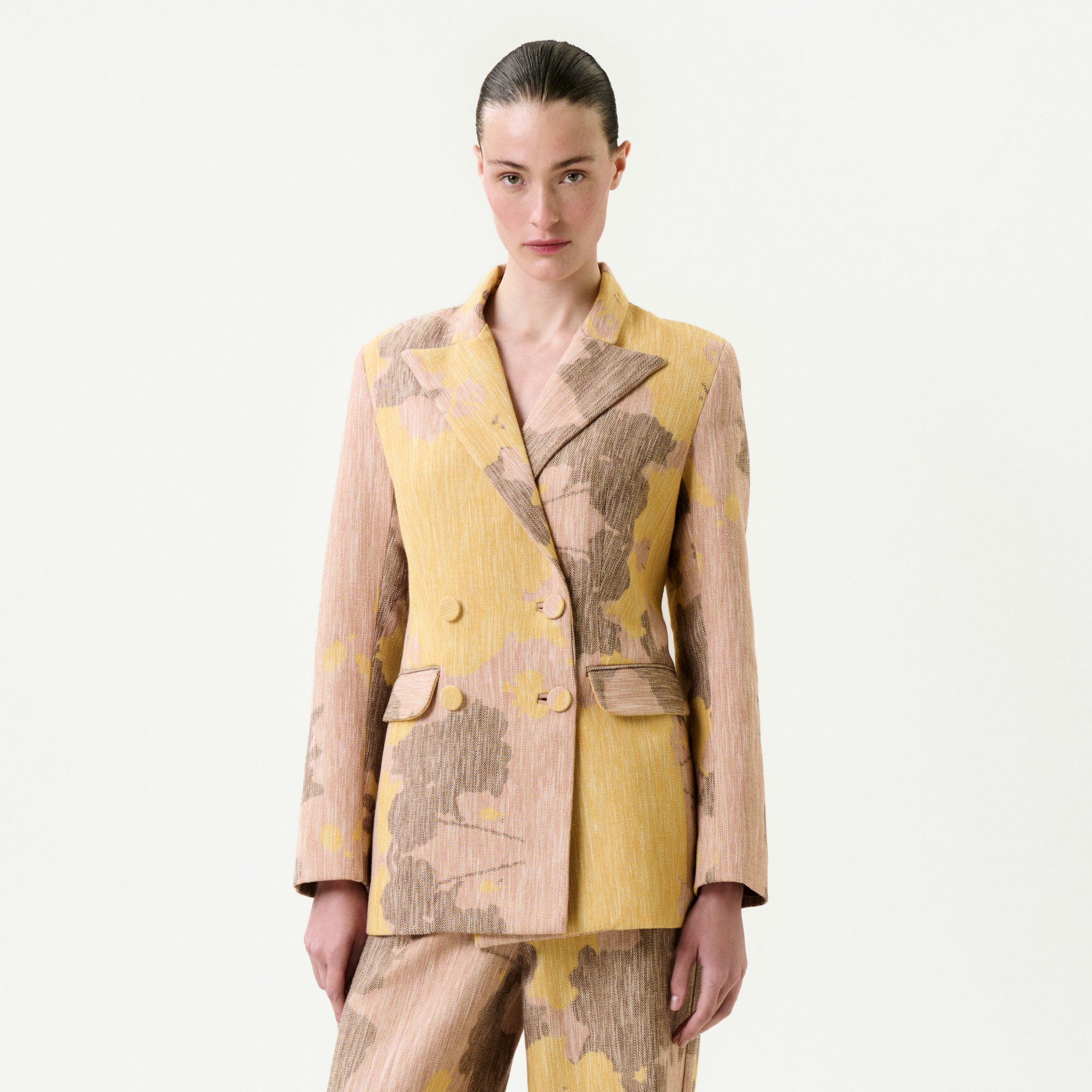 A person with slicked-back hair models the Frankie Jacket—yellow and beige floral Italian fabric, true to size—with matching pants, posing against a white background.