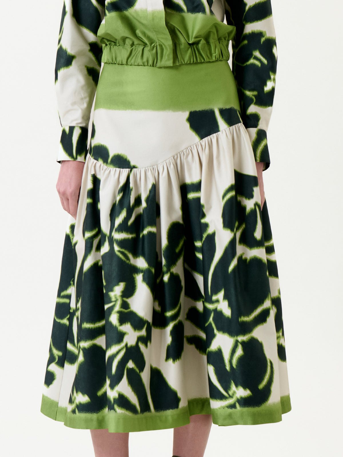 A person wearing the Libby Skirt, featuring a green and white tie-dye pattern with a gathered waist and flared hem; only the lower torso and upper legs are visible.
