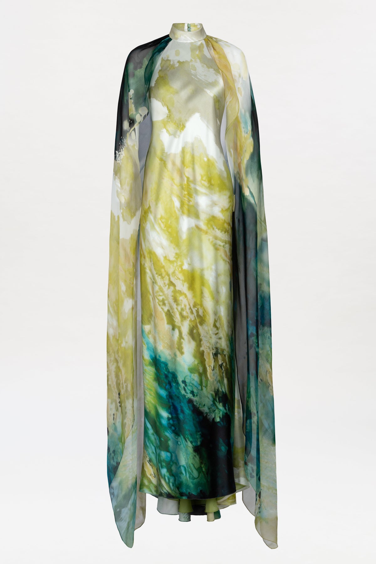 Discover the Sabina Dress: a flowing, floor-length gown adorned with a watercolor-inspired pattern in yellow, green, blue, and black. This elegant design is completed with a sheer, matching cape draped gracefully over the shoulders.