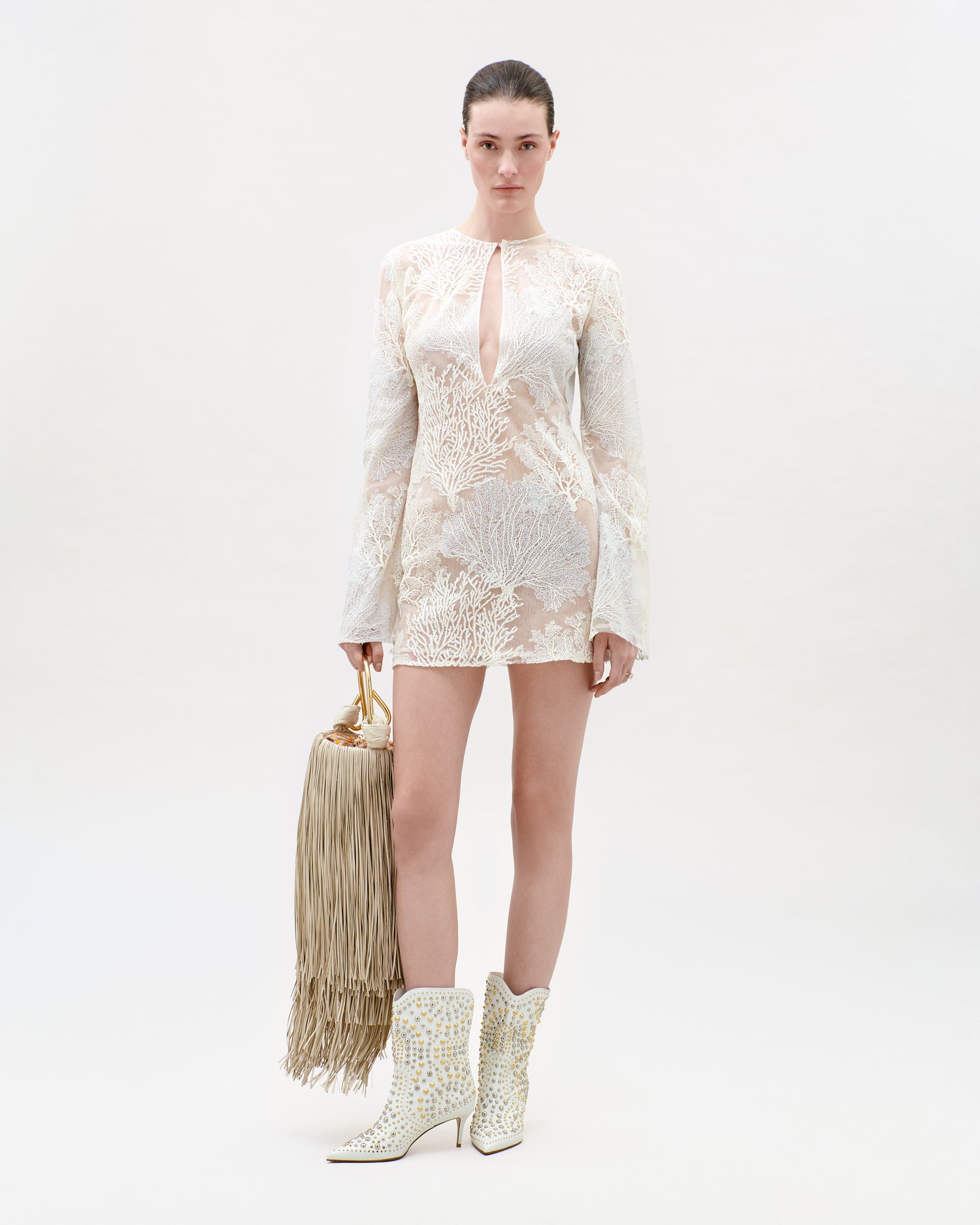 Woman wearing a white lace dress and white boots with a beige handbag on a light gray background
