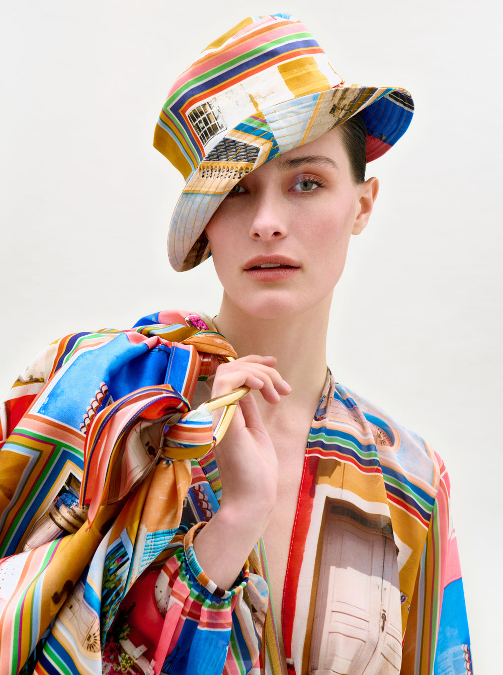 A woman poses with her hand near her face, one eye partly hidden by the brim of the Dama Bucket Hat, featuring vibrant geometric and architectural designs from Colombia.