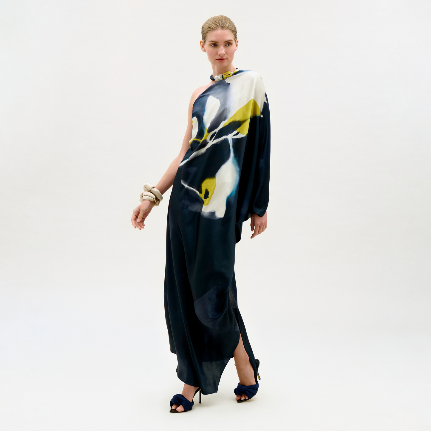 Woman wearing a long, dark blue dress with abstract white and yellow patterns on a white background