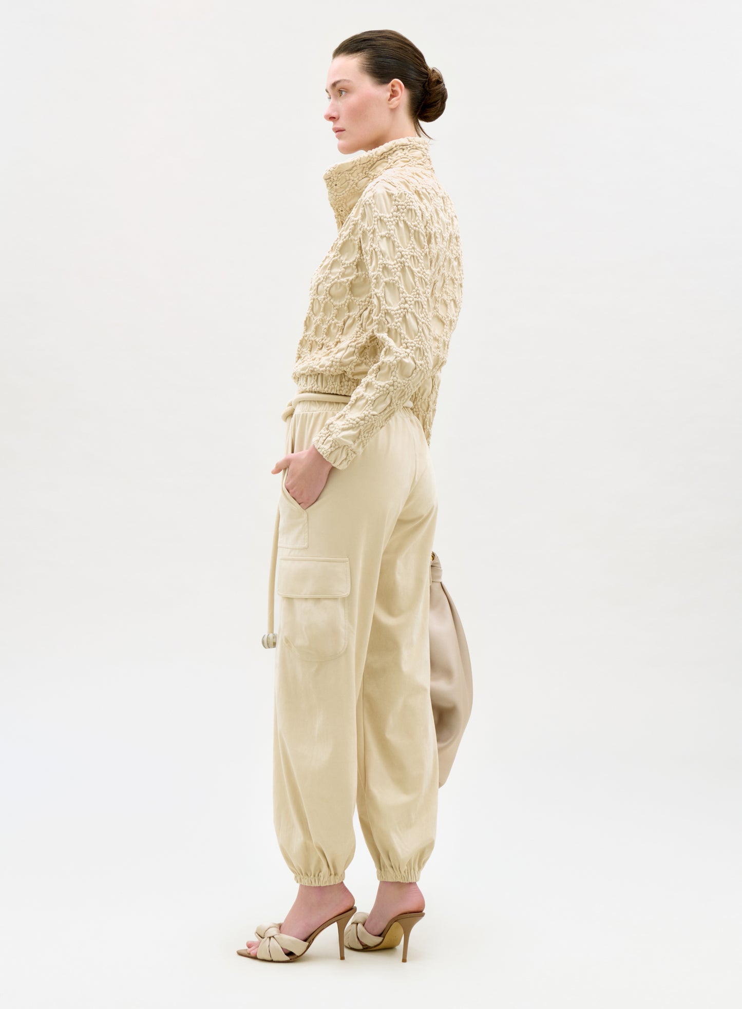 Woman wearing a beige knit cardigan and matching pants on a white background