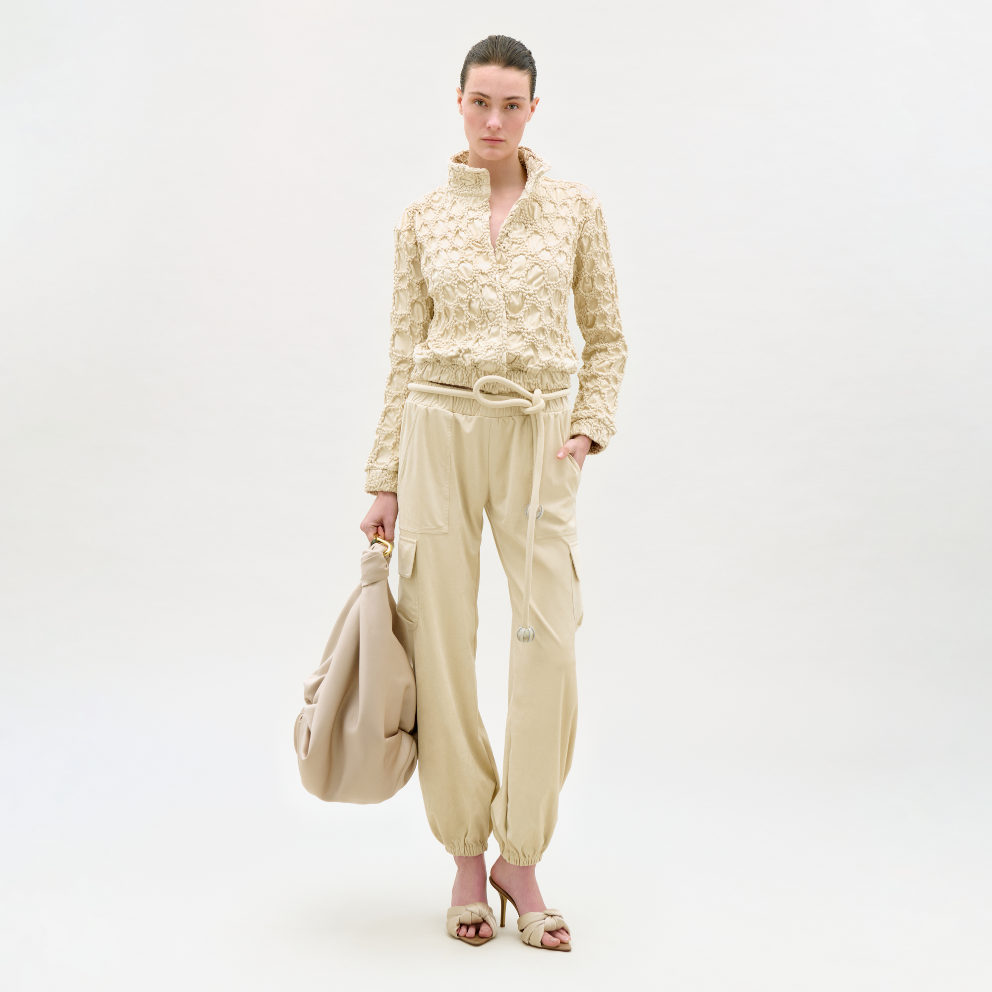 Woman wearing a beige outfit with a matching bag on a white background