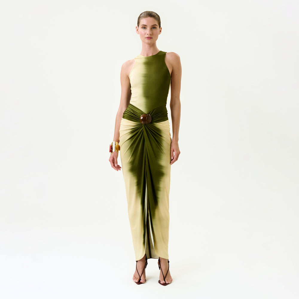 A woman poses against a white background in the Leni Dress—a sleeveless, gradient green-to-yellow midi dress from Colombia with a gathered knot waist—styled with bracelets and strappy sandals.