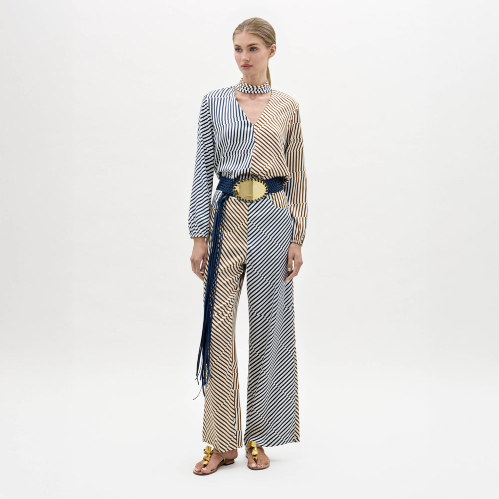 A woman stands against a plain background wearing the Emine Pant, styled with gold sandals and a matching choker.