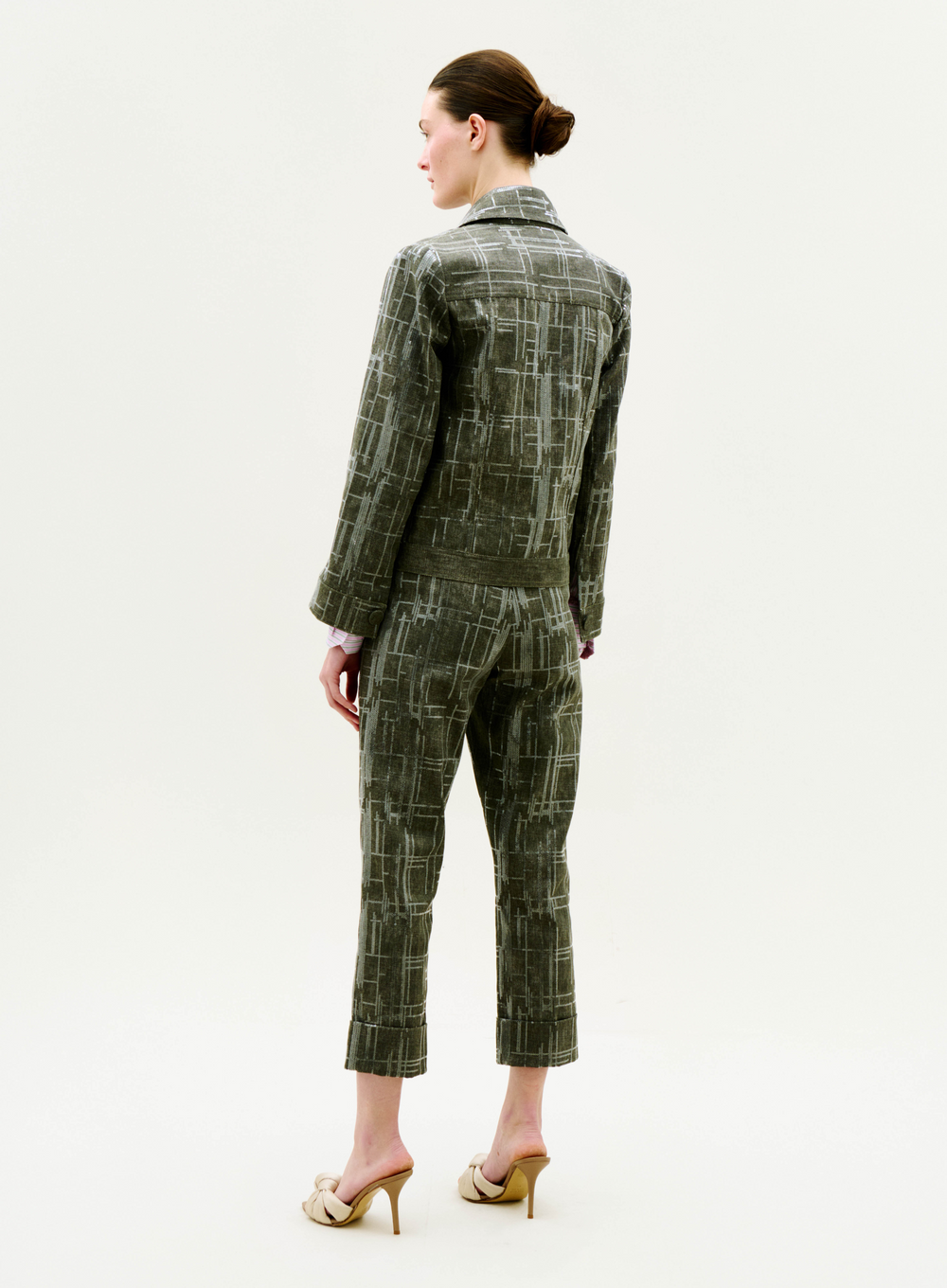 A woman stands facing away in the green plaid Moad Pant with a matching jacket, her hair in a neat bun and wearing beige high-heeled shoes against a plain white background.