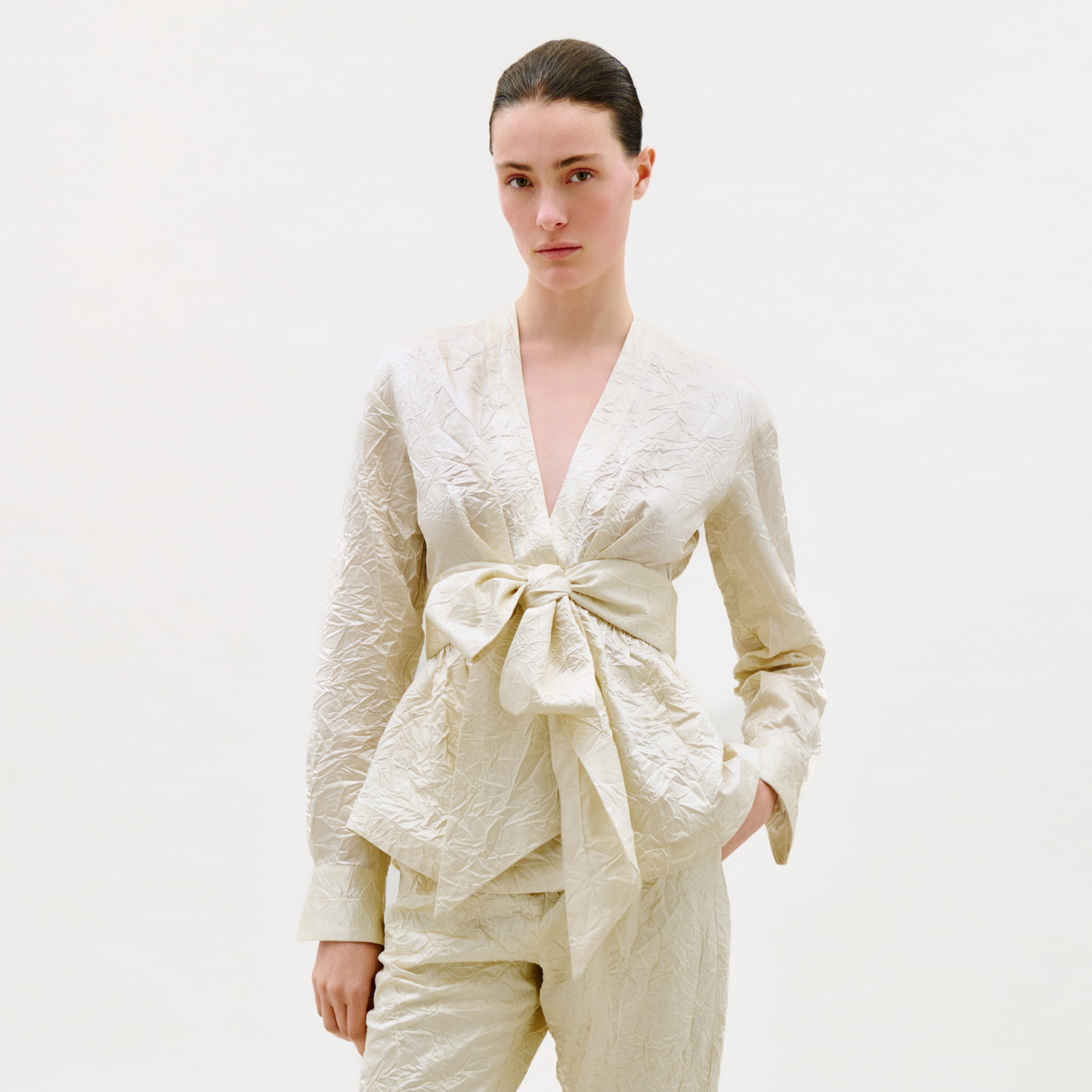 Woman wearing a cream-colored outfit with a tie detail on a white background