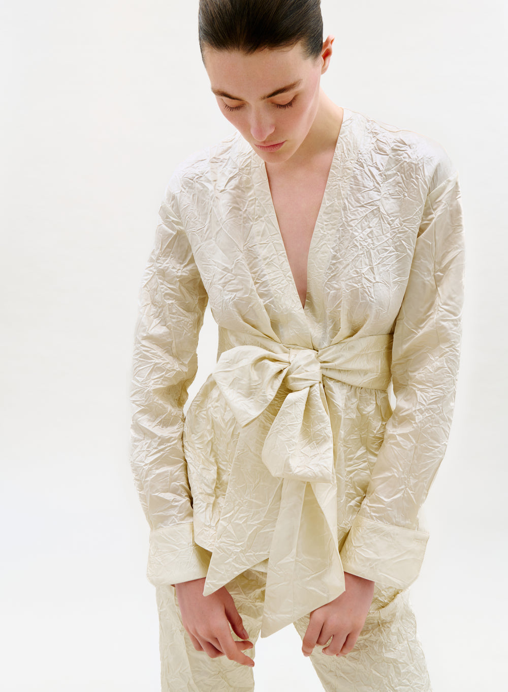 Woman wearing a cream-colored textured outfit with a bow detail on a white background