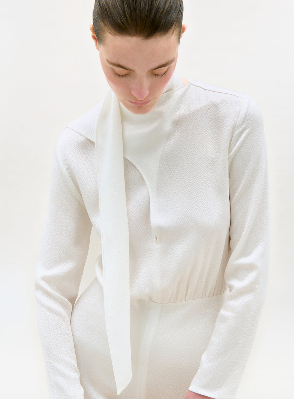 Person wearing a white outfit with a long white scarf against a light background