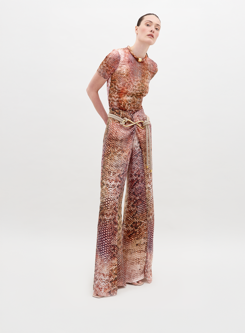 Person wearing a snakeskin-patterned outfit, consisting of a short-sleeve top and high-waisted, wide-leg Canturipe Pant Peach Animal Print, standing against a plain white background. This chic ensemble is available for pre-order and will ship by November 15th, 2024.