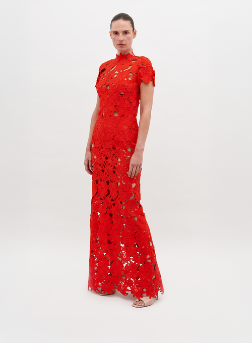 Person wearing a floor-length, red lace Taiana Dress Rouge with a high neckline and short sleeves, standing against a plain white background. Pre-order now to ensure delivery by the November 15th, 2024 ship-by date.