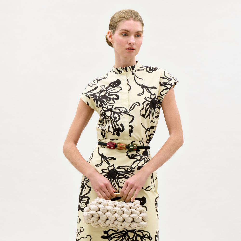 Woman wearing a black and white floral dress holding a textured handbag on a white background