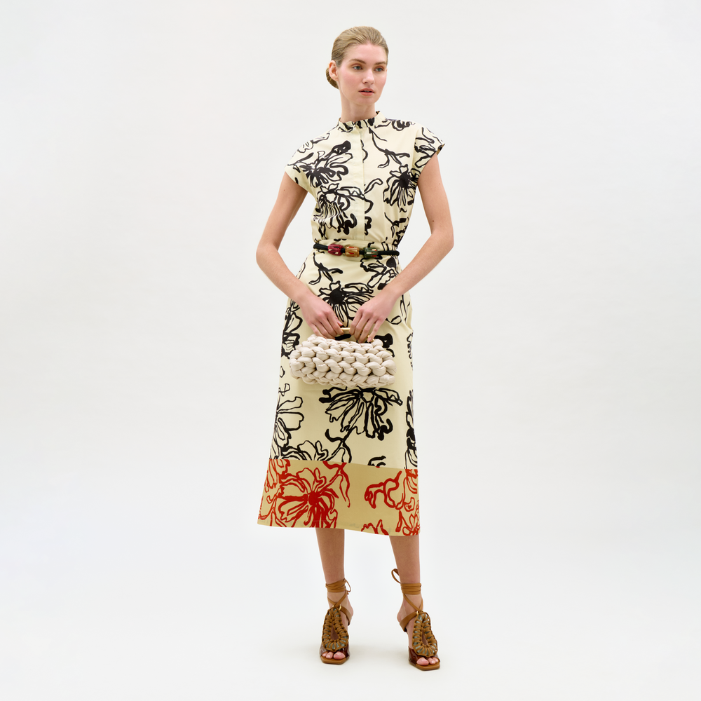 Woman wearing a patterned dress holding a textured handbag on a white background