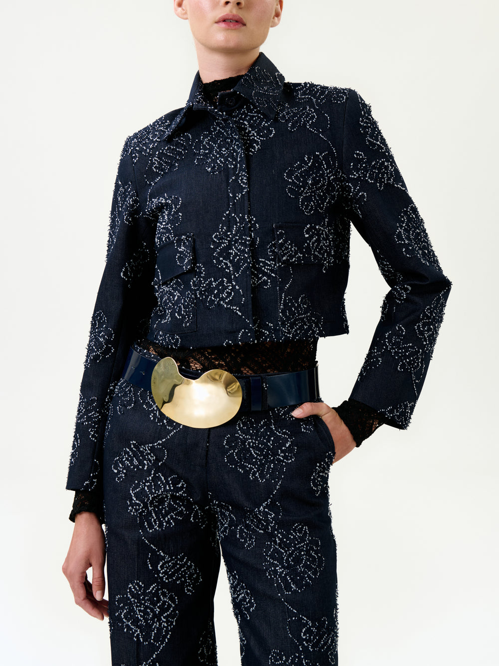 Person wearing a dark blue patterned outfit with a gold belt on a white background