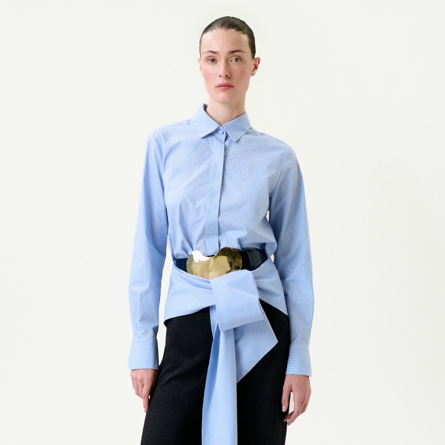Person wearing a light blue shirt with a gold belt and black pants on a white background