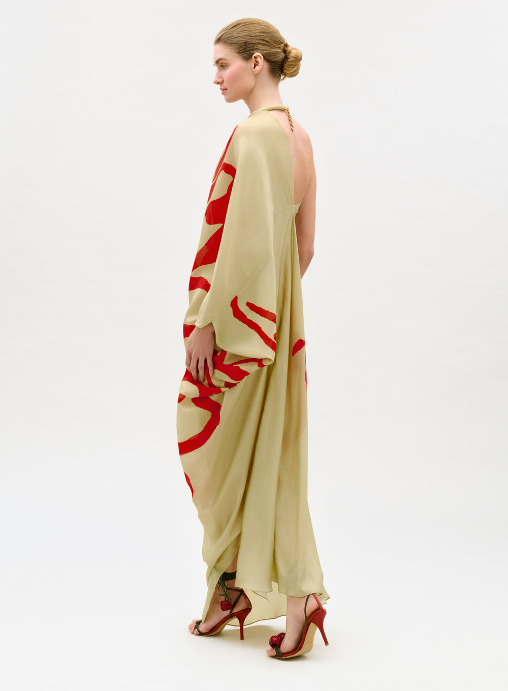 Woman wearing a long, light-colored dress with red abstract patterns on a white background