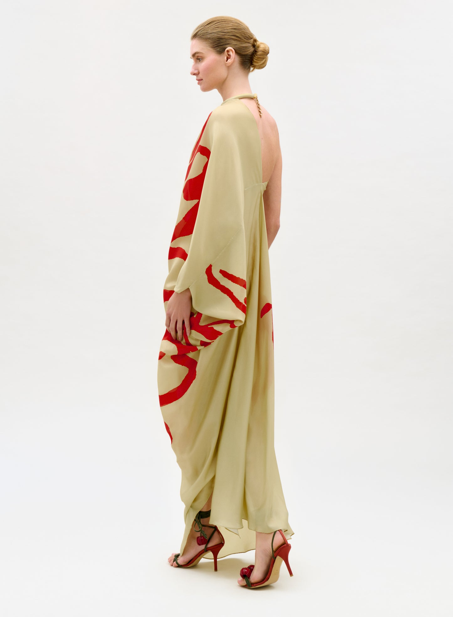 Woman wearing a long, light-colored dress with red abstract patterns on a white background