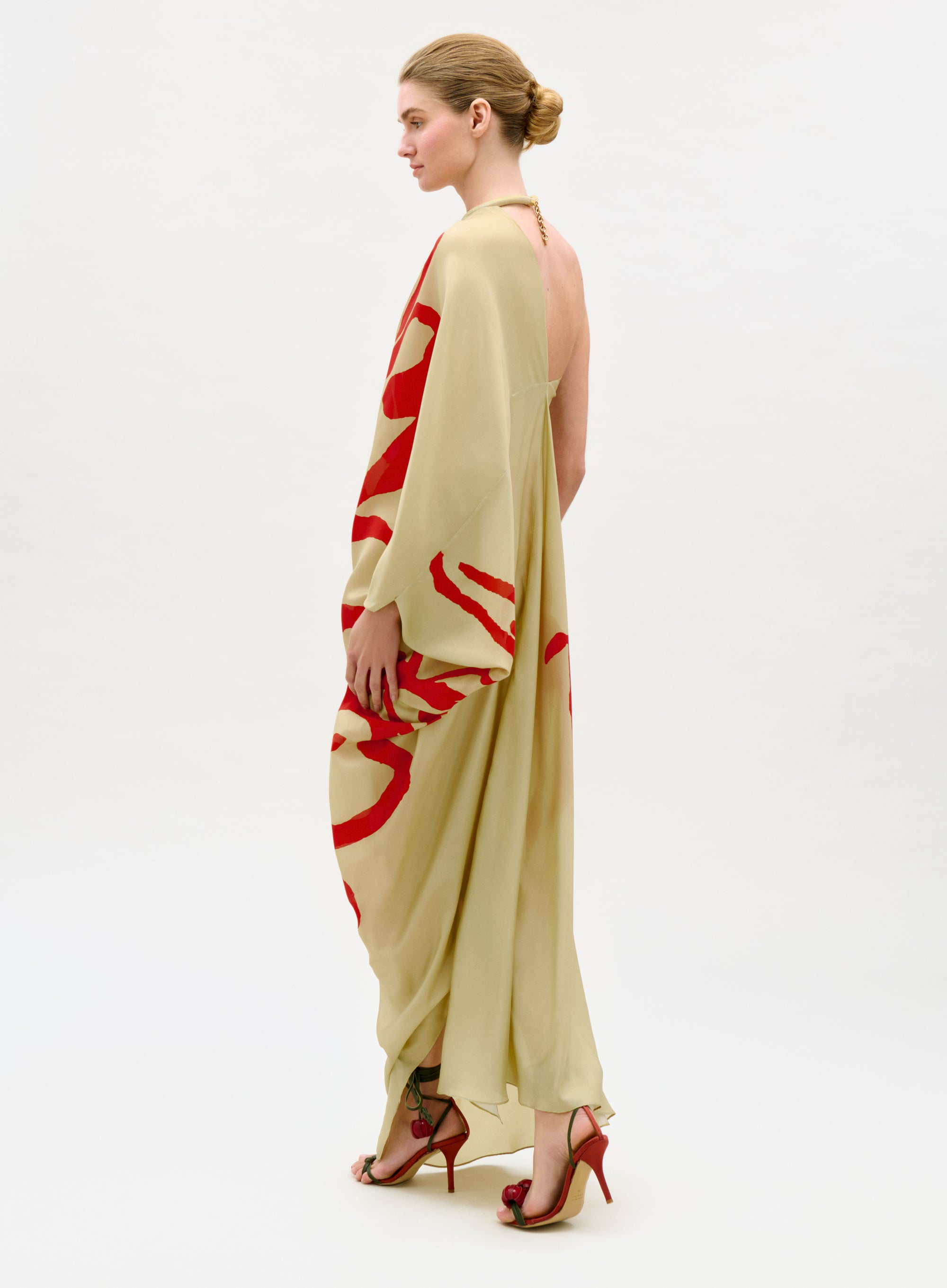 Woman wearing a long, light-colored dress with red abstract patterns on a white background