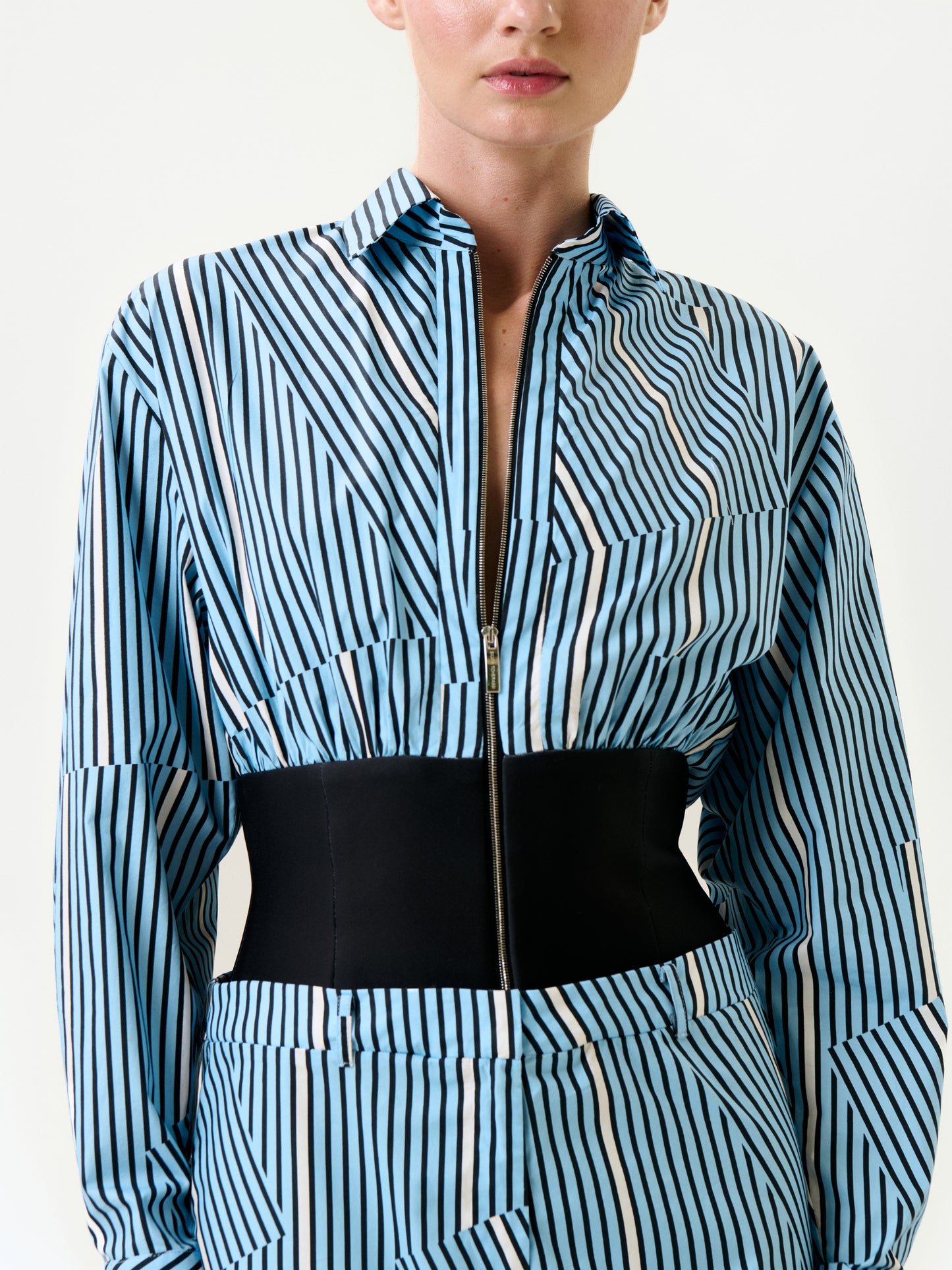 The Lorena Dress, shown from shoulders to hips against a plain background, features blue and white vertical stripes, premium Italian fabric, a black wide belt, and a zip-up front.