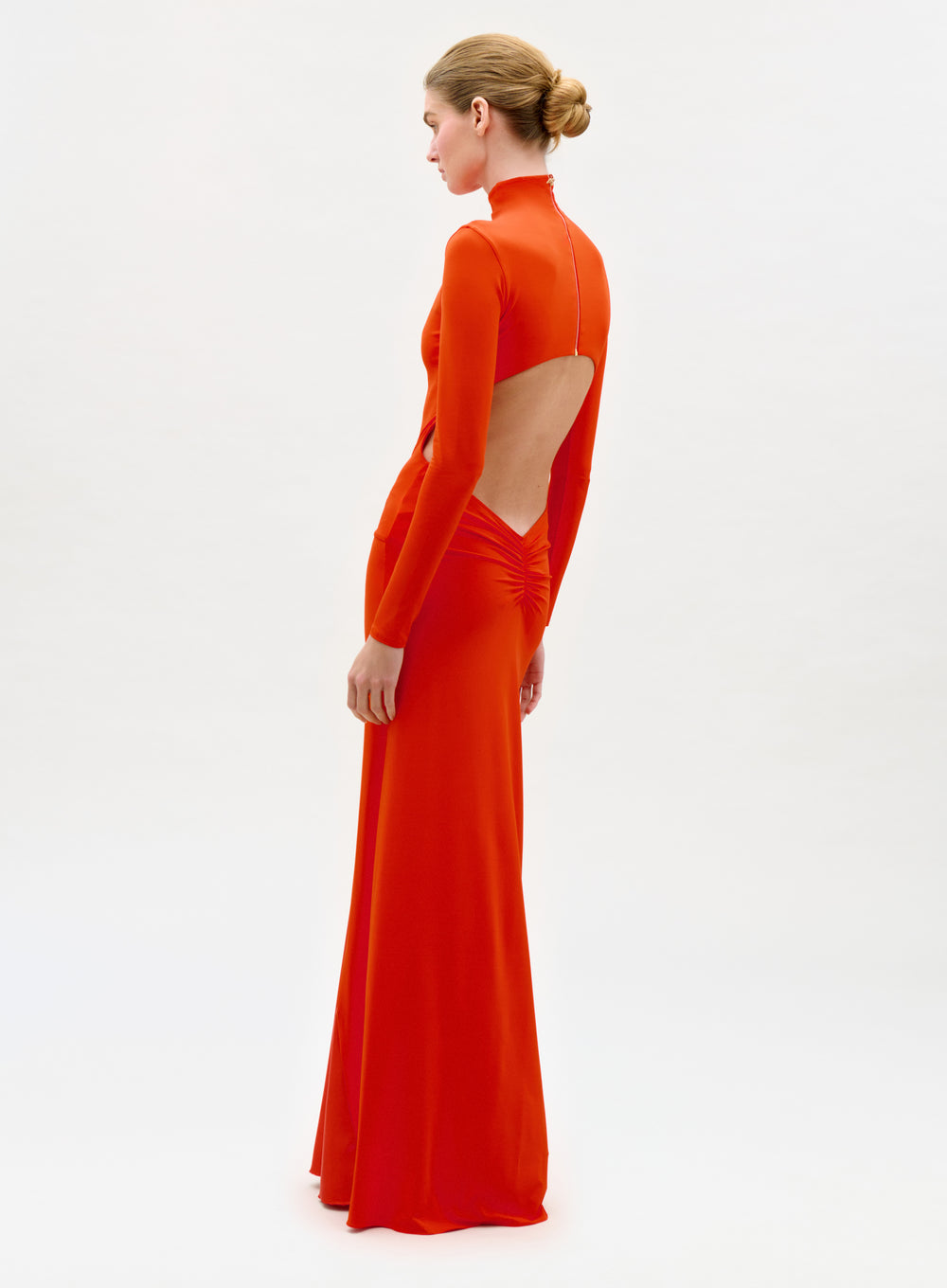 Woman wearing a bright orange long-sleeve gown with cut-out design on a white background