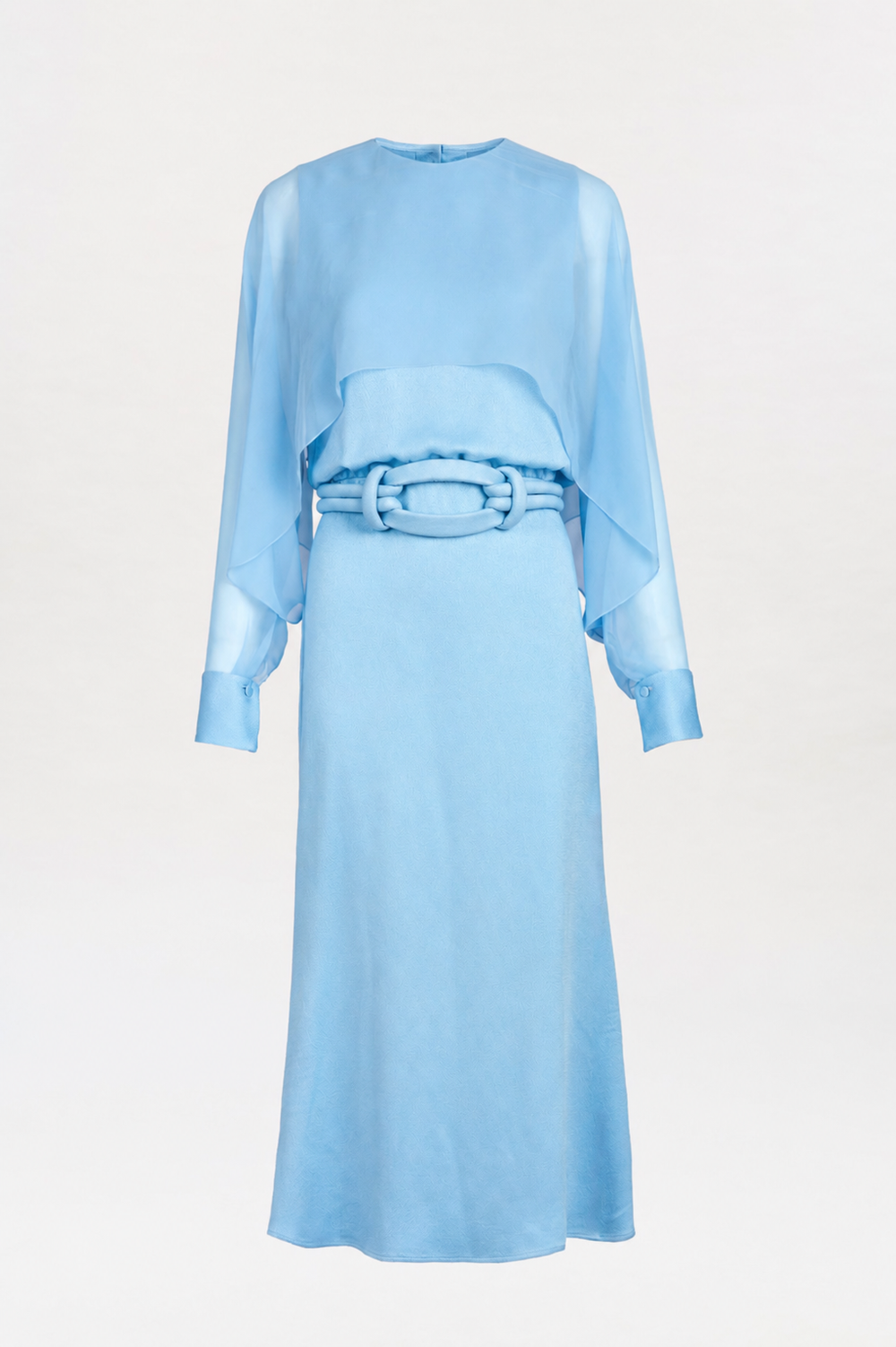 The Rubina Dress is a light blue, long-sleeved dress featuring a layered top, wide cuffs, and a textured belt at the waist. It has a simple neckline and a mid-length skirt, and is displayed on a plain white background.