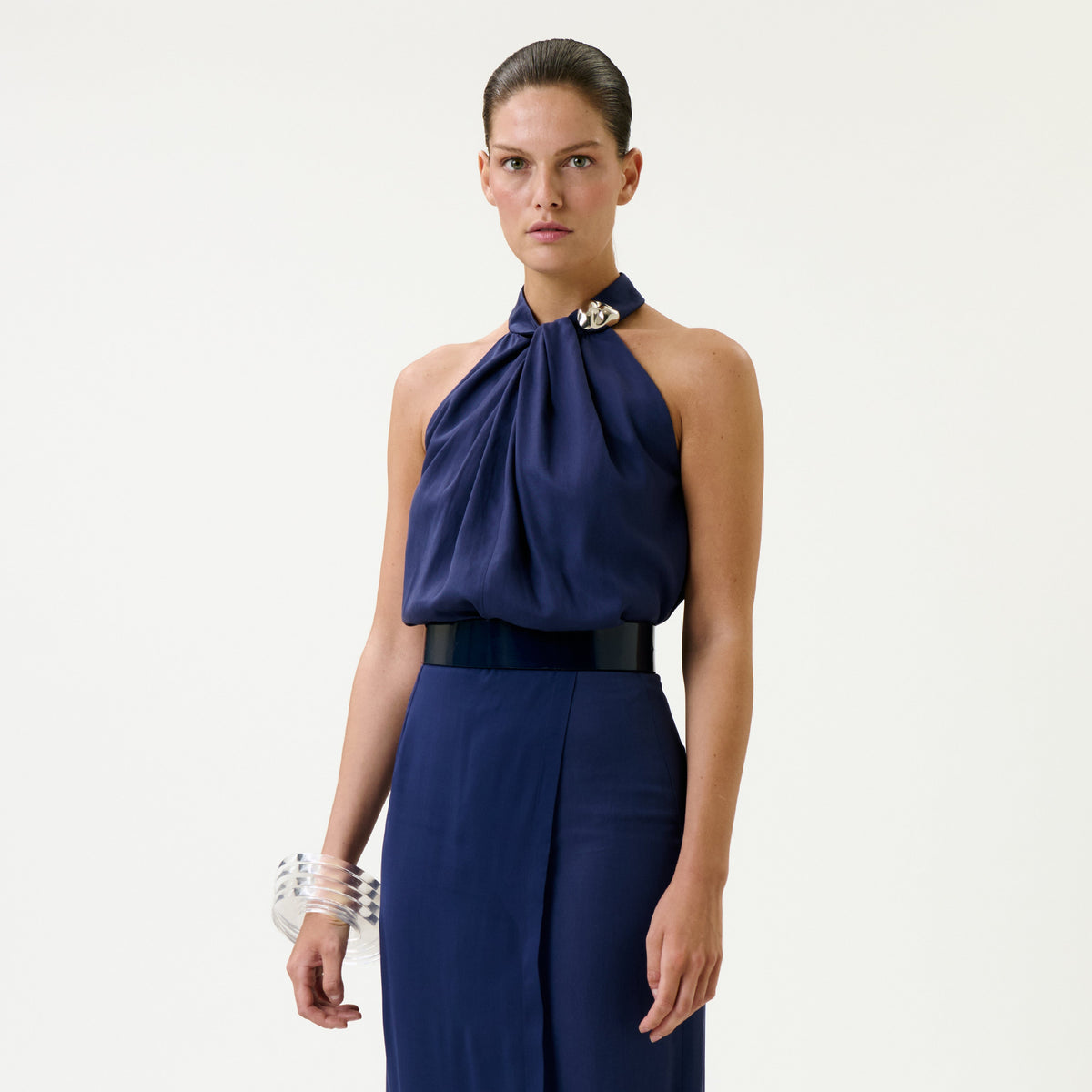 Wearing the Shela Blouse, a woman stands against a plain background, styled with a matching skirt, wide black belt, and clear bangles.