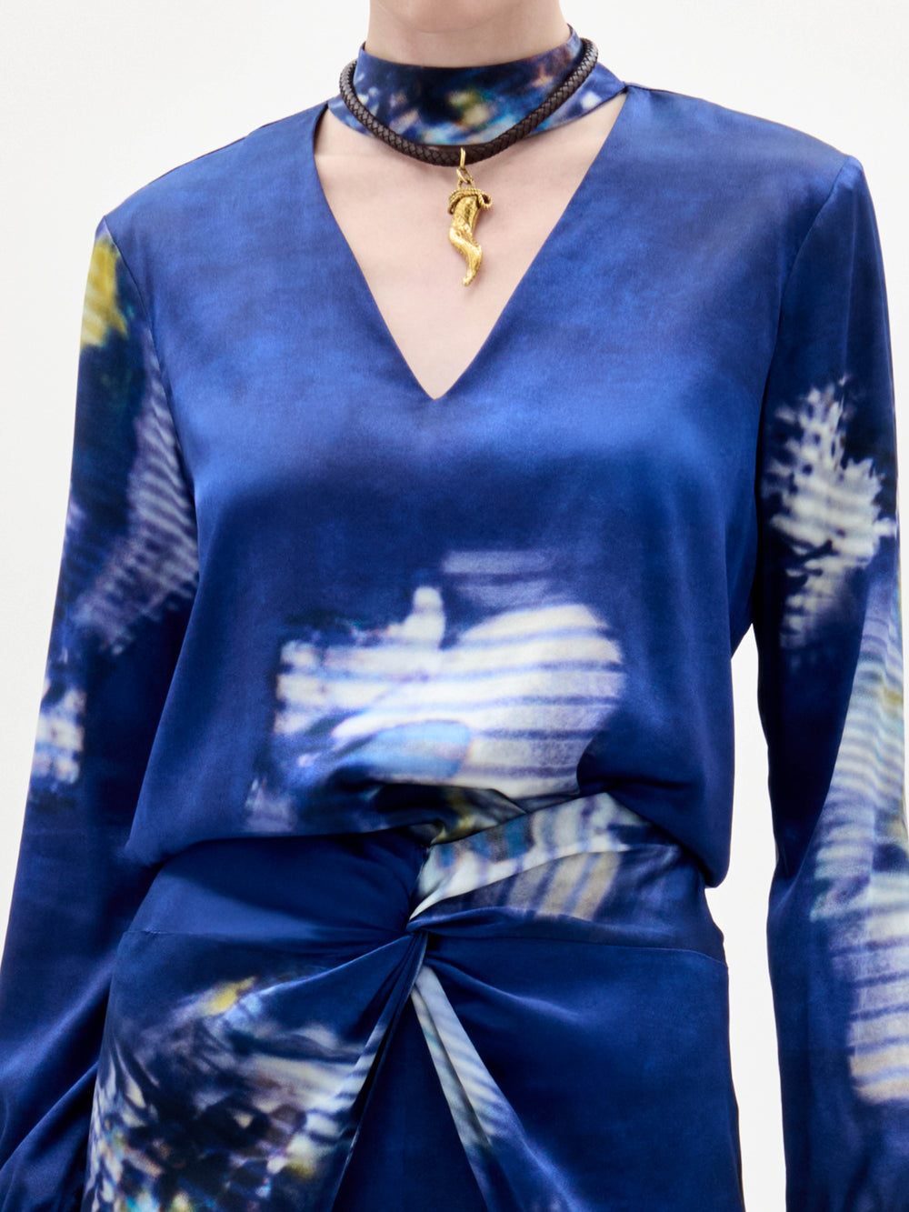 Woman wearing the Lane Blouse, a blue patterned top, paired with a matching skirt and choker necklace, standing against a plain light background.