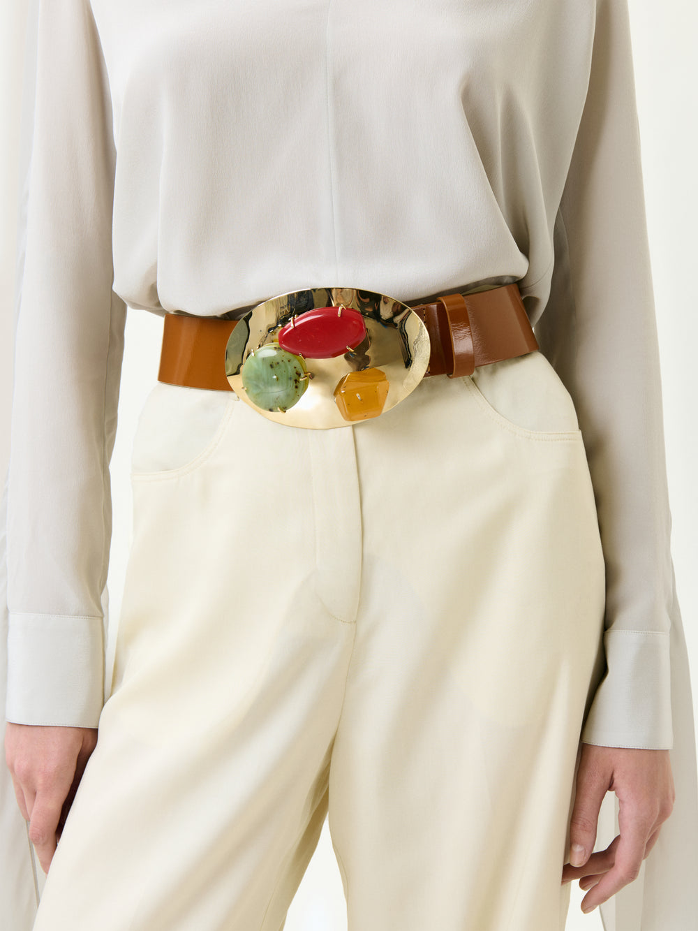 Wearing the Emine Pant in cream, styled with a light Italian-fabric blouse and a wide brown belt featuring a large gold buckle adorned with colorful stones.