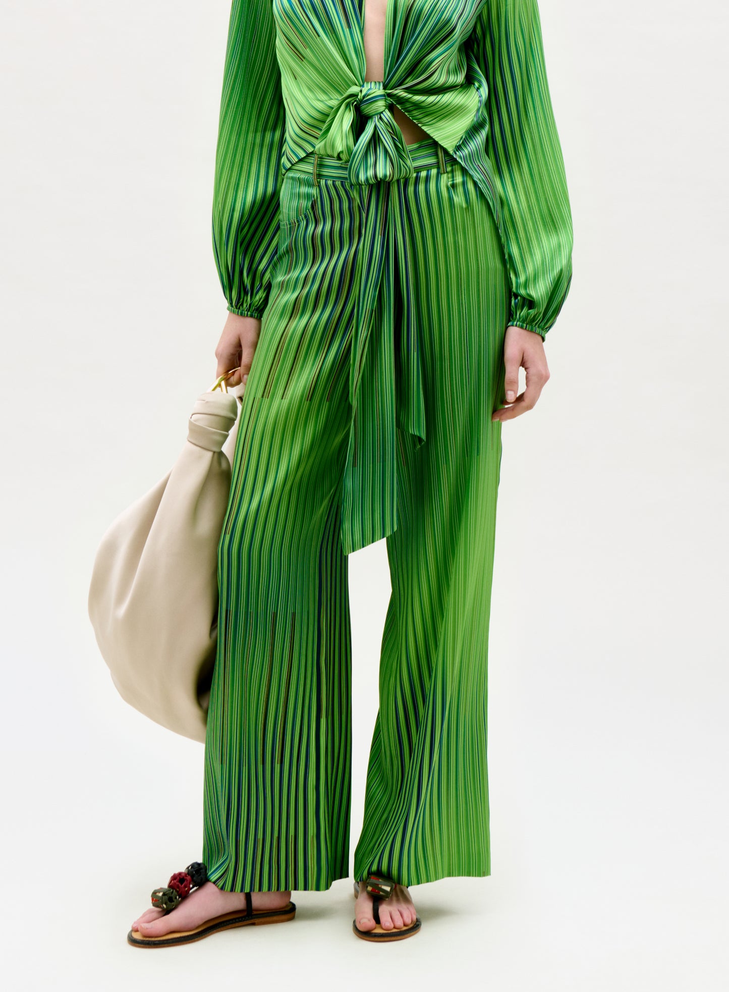 Person wearing a green pleated outfit holding a beige bag on a white background