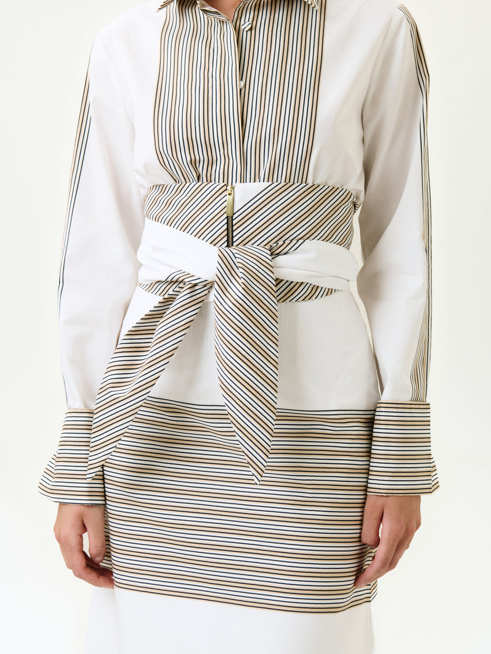 A person wears the Angeles Shirt, a 100% cotton white shirt with vertical brown and black stripes, paired with a matching striped skirt and a wide striped belt at the waist. Only the torso and arms are shown.