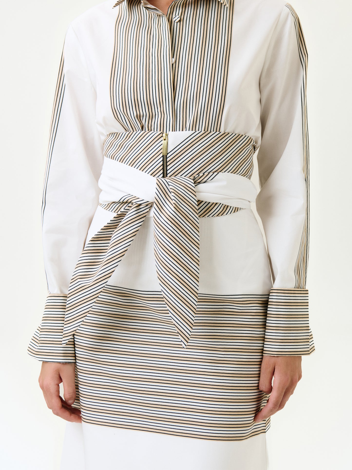 A person wearing the Lyla Skirt, featuring horizontal stripes and bold waistband details, paired with a white shirt with thin black and gold vertical stripes in 100% Italian cotton and a wide detachable belt tied at the waist.