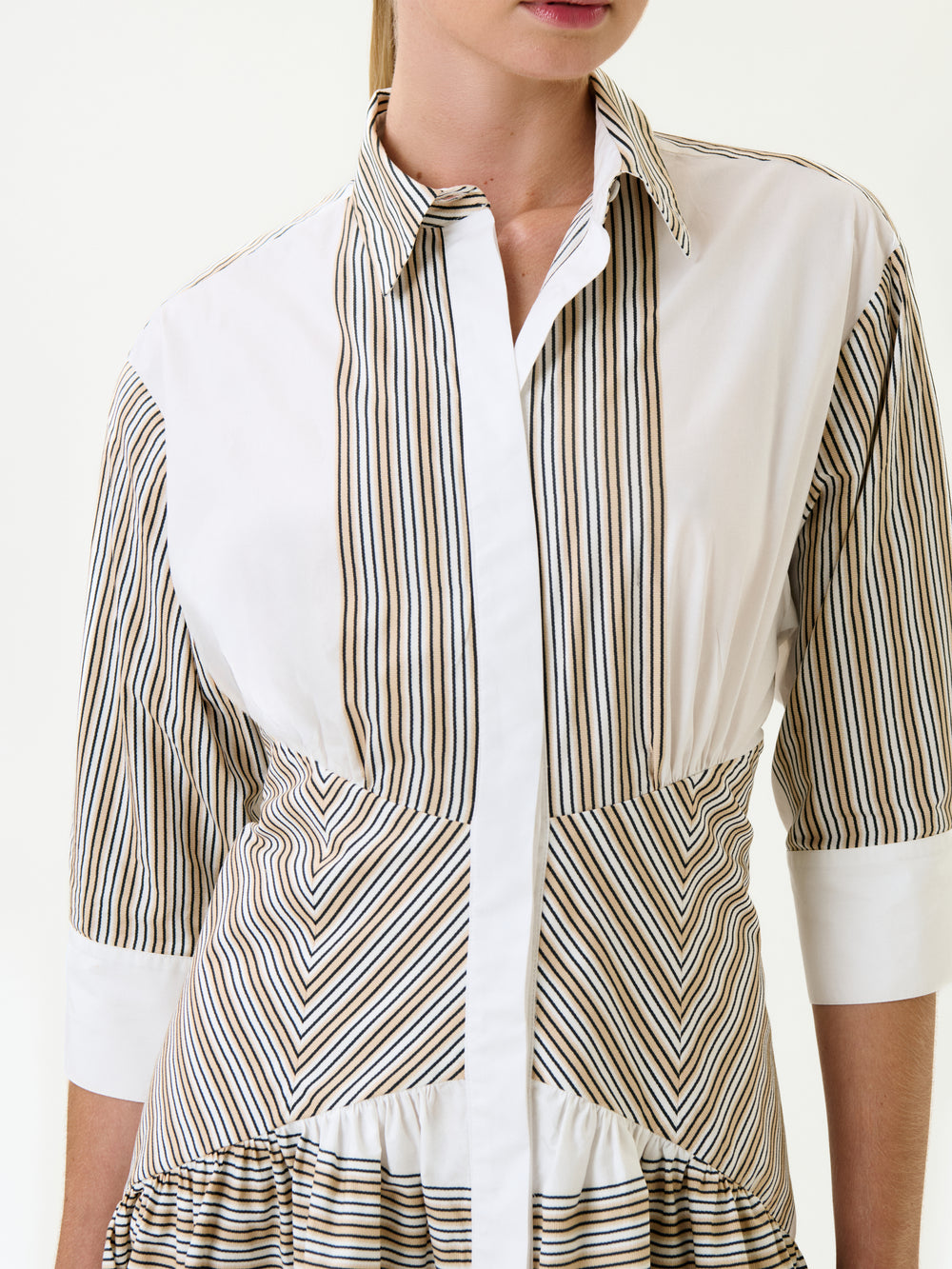 The woman wears the Indy Dress, a white button-up midi dress with vertical and diagonal brown and black stripes in 100% Italian cotton. Featuring a collared neckline and three-quarter sleeves, her face is partially out of frame.