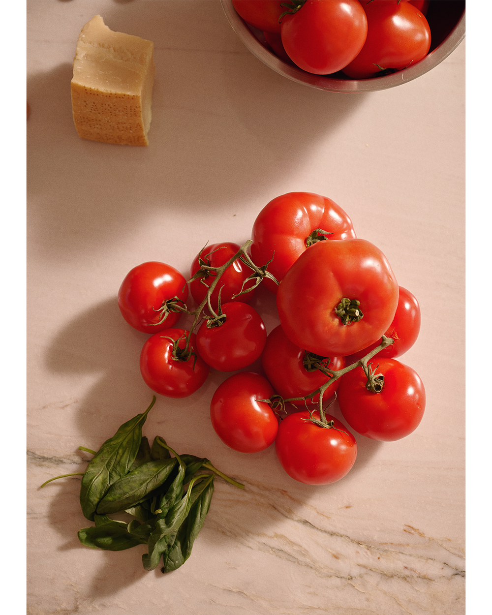 Red tomatoes on a marble surface with basil and Parmesan cheese.
